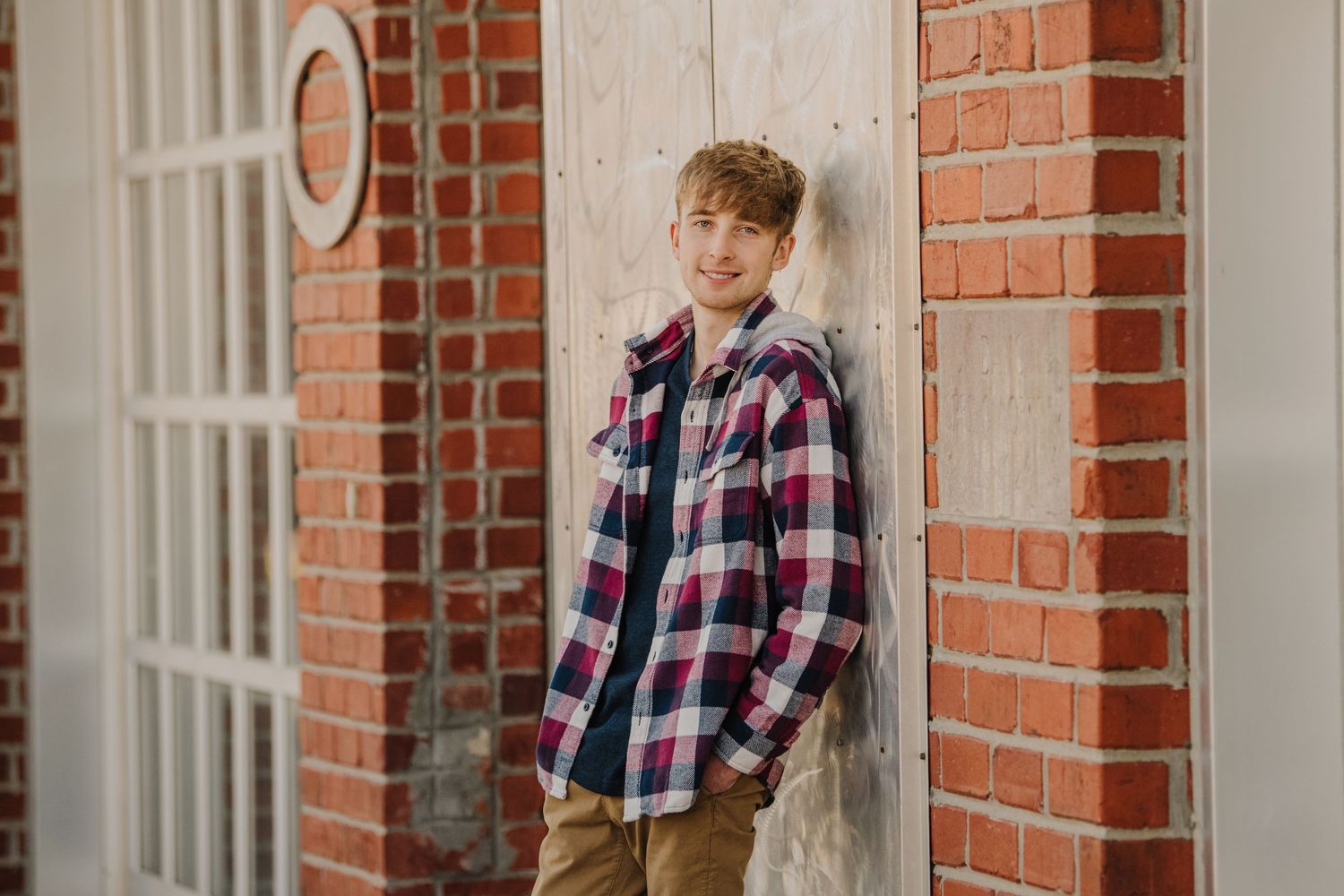 Casual portrait series against a brick wall featuring plaid shirt and relaxed poses.