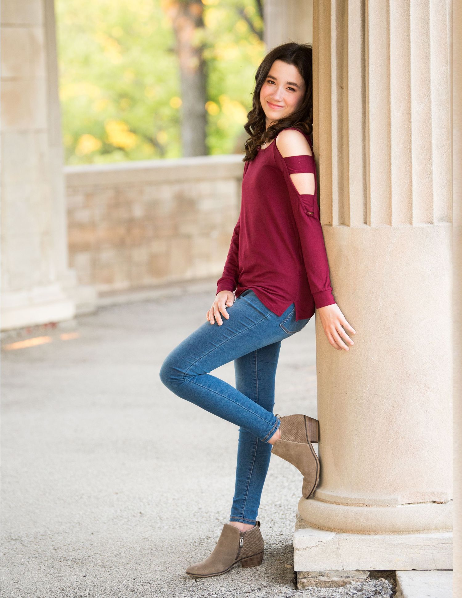 Woman in burgundy sweater and jeans posing against white columns outdoors.