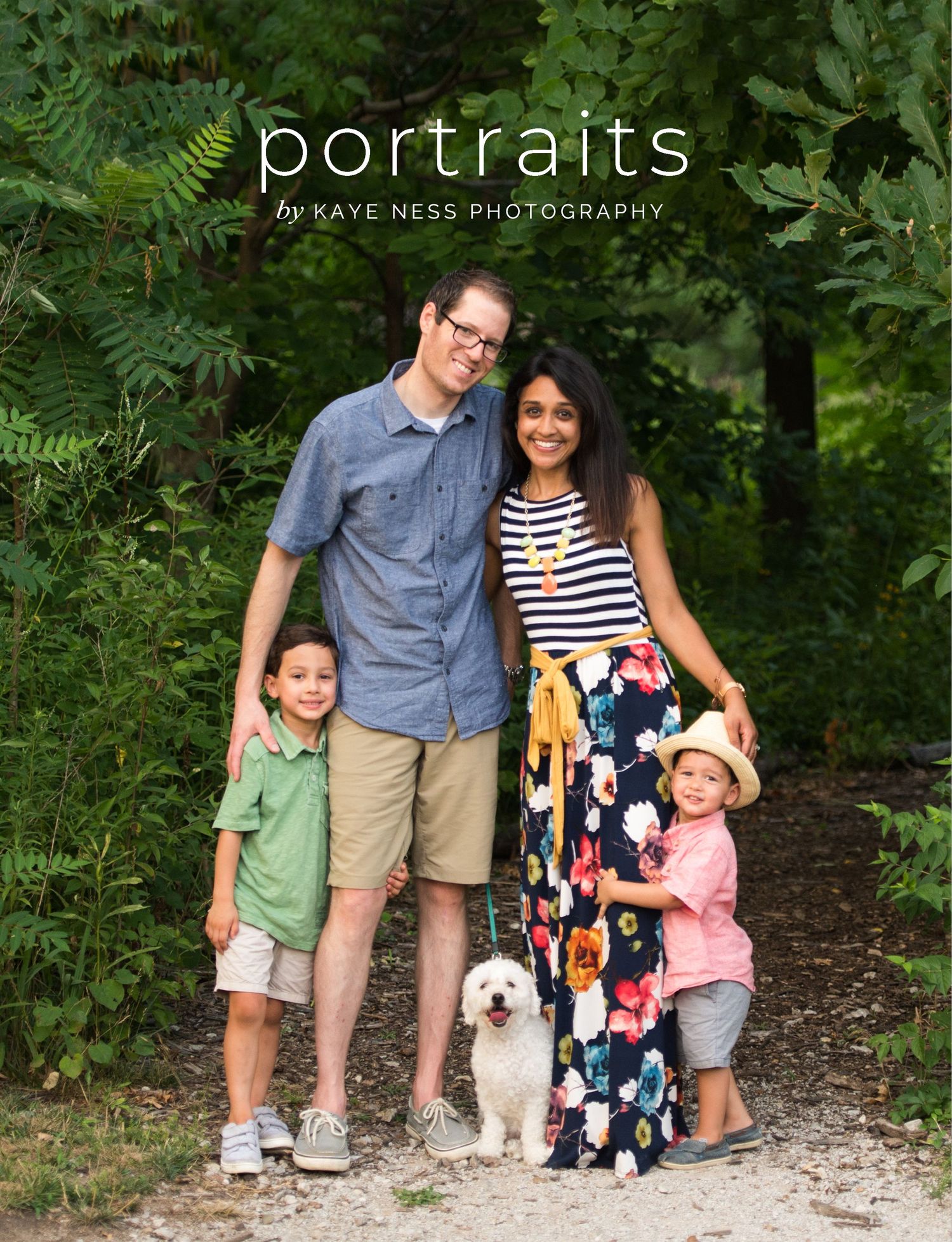 Family portrait session with parents, children and dog posing outdoors among green foliage.