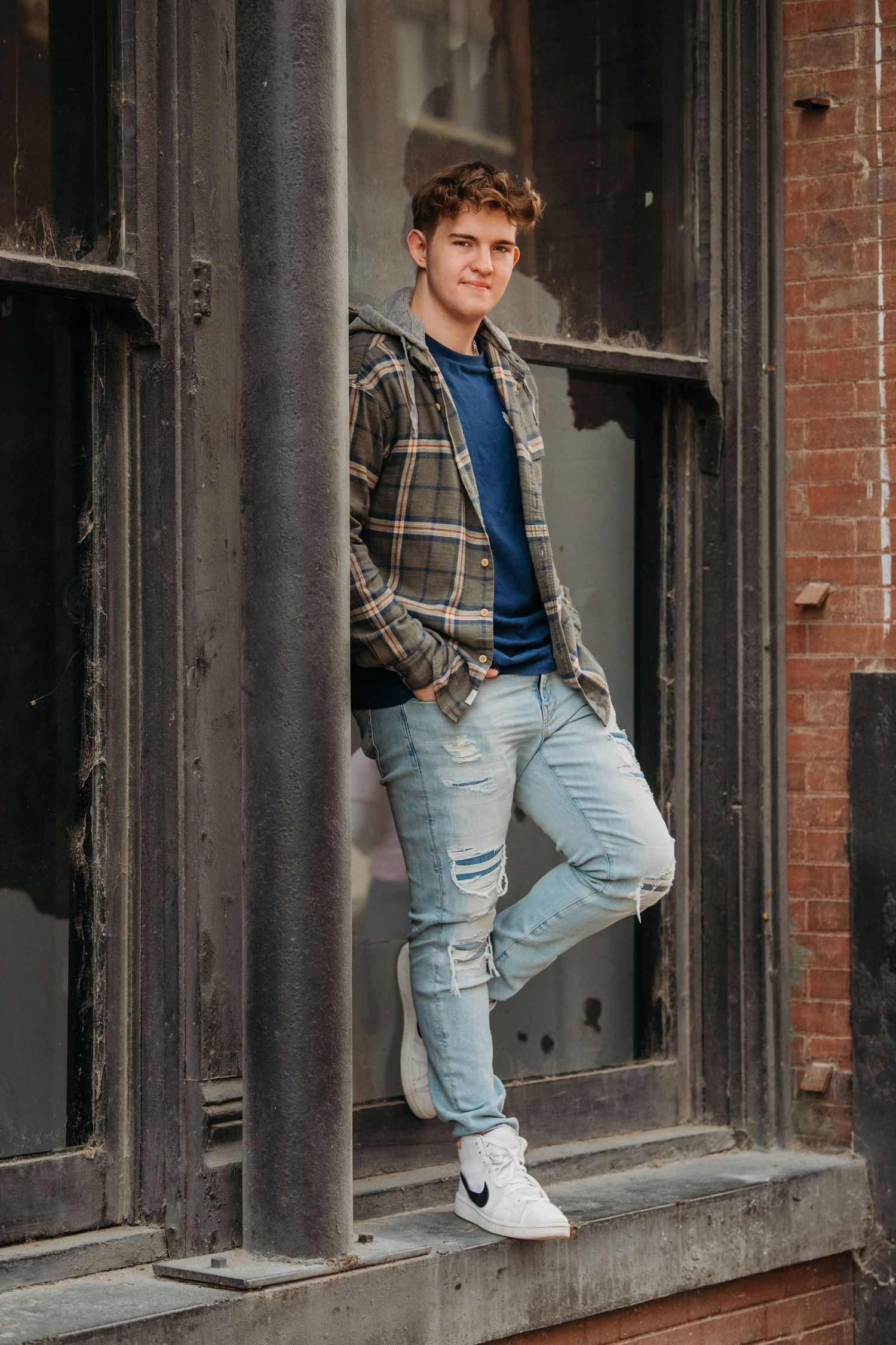 Urban portrait against industrial brick building with metal window frames.