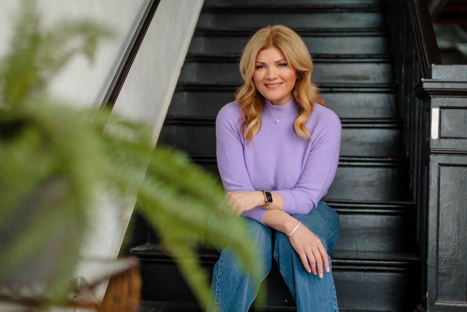 Casual outdoor portrait of someone wearing a purple sweater and jeans on dark steps.