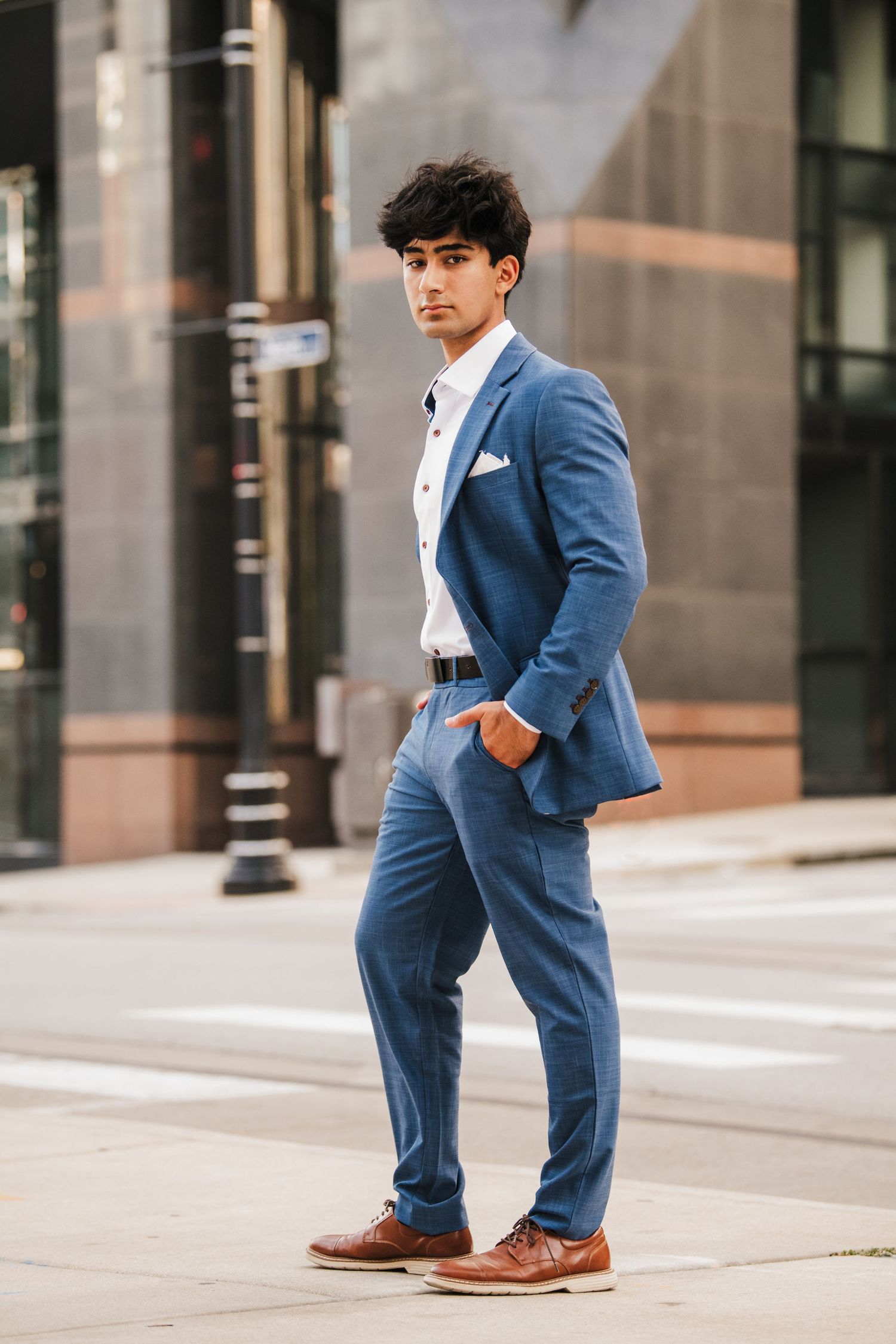 Professional headshots of someone in blue suit walking on urban sidewalk.