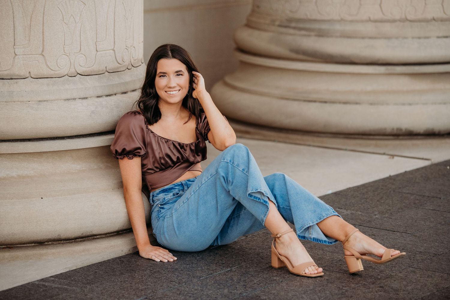 Casual portraits in brown top and denim against classical architecture.