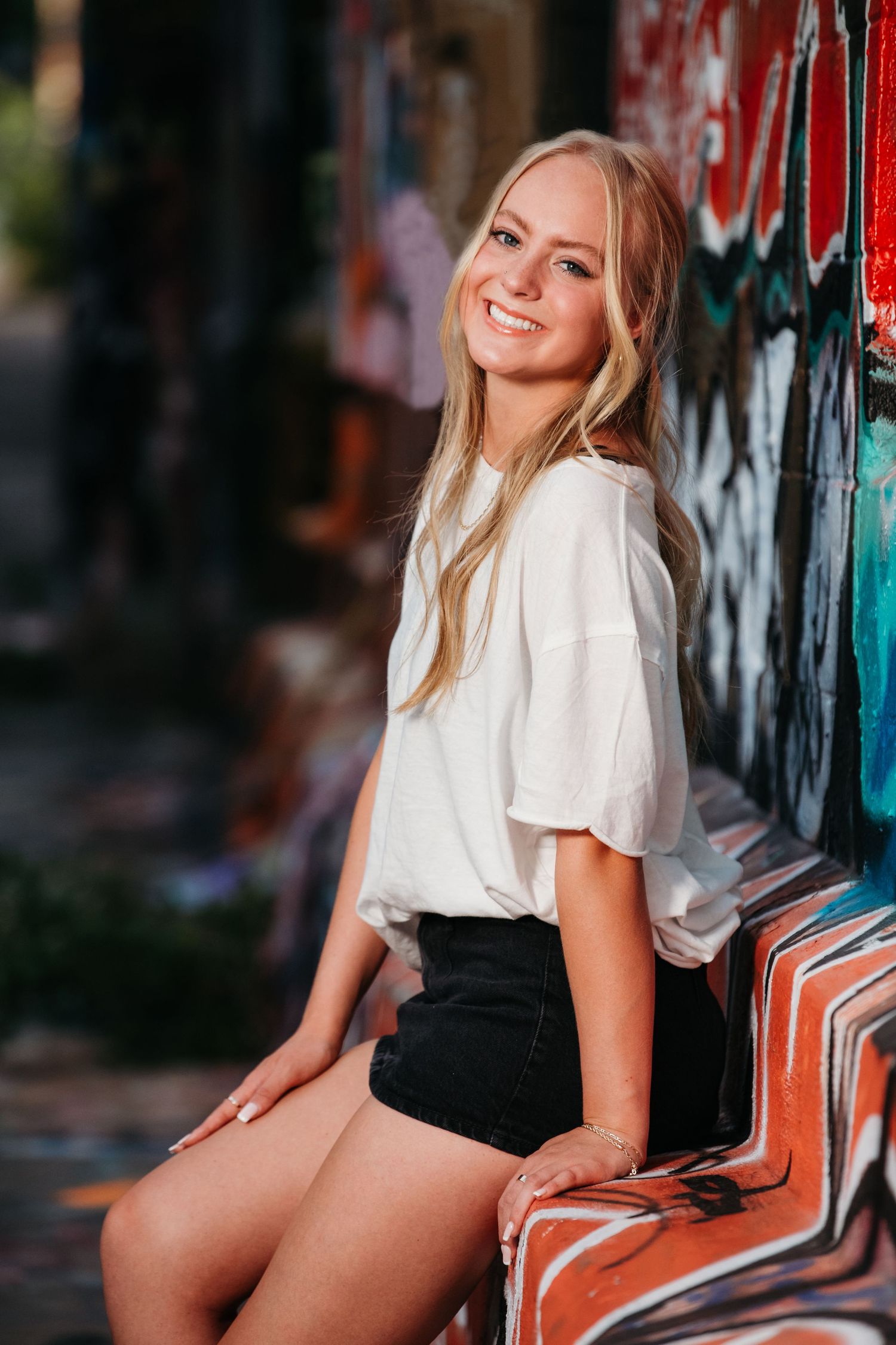 Urban fashion portraits with white top and black shorts against colorful graffiti wall.