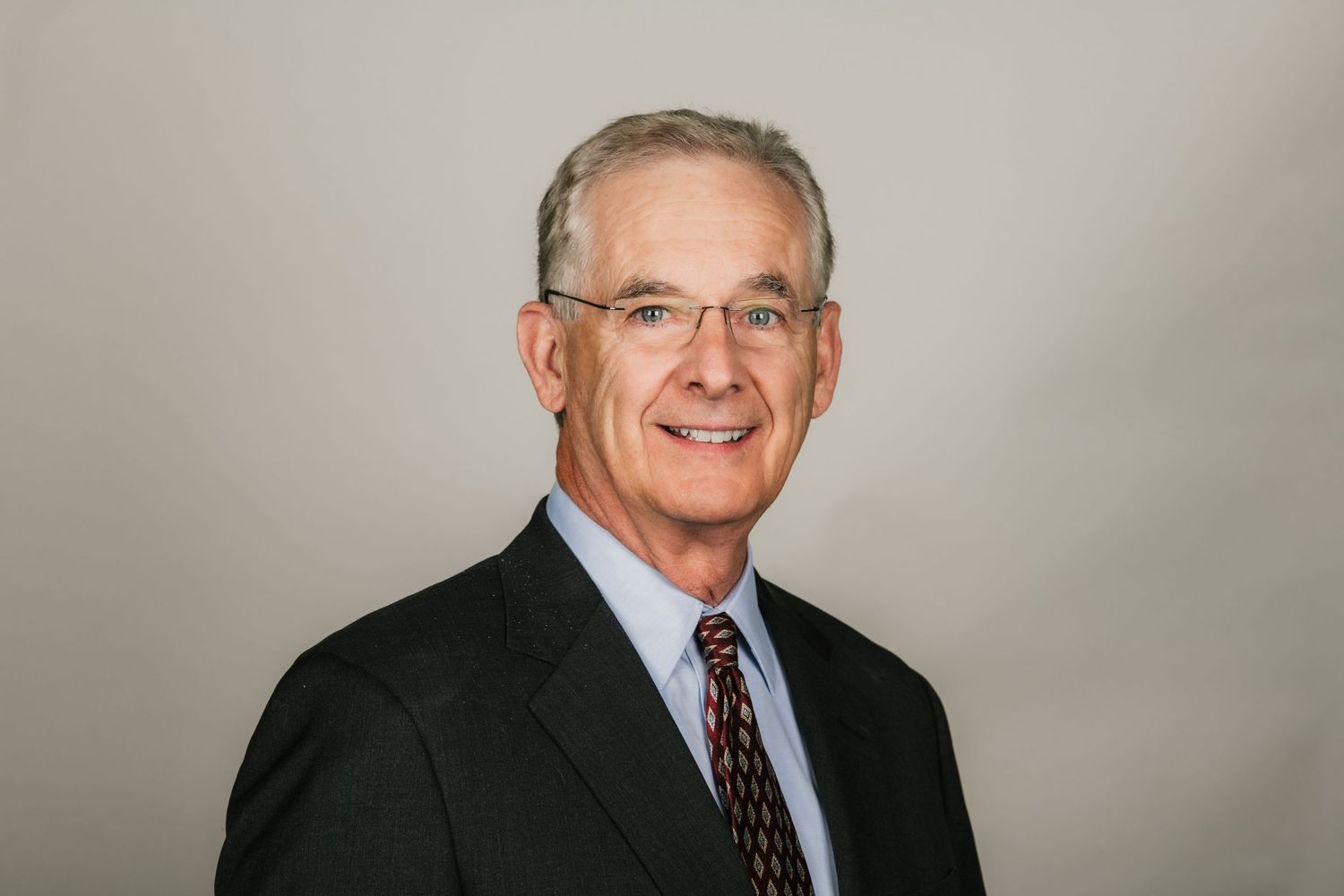 Professional business portrait of man in glasses and suit against gray background.