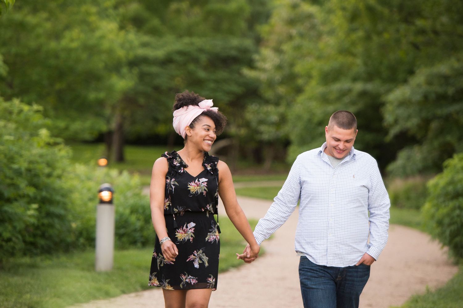A couple walks hand in hand along a tree-lined path in a park during summer.