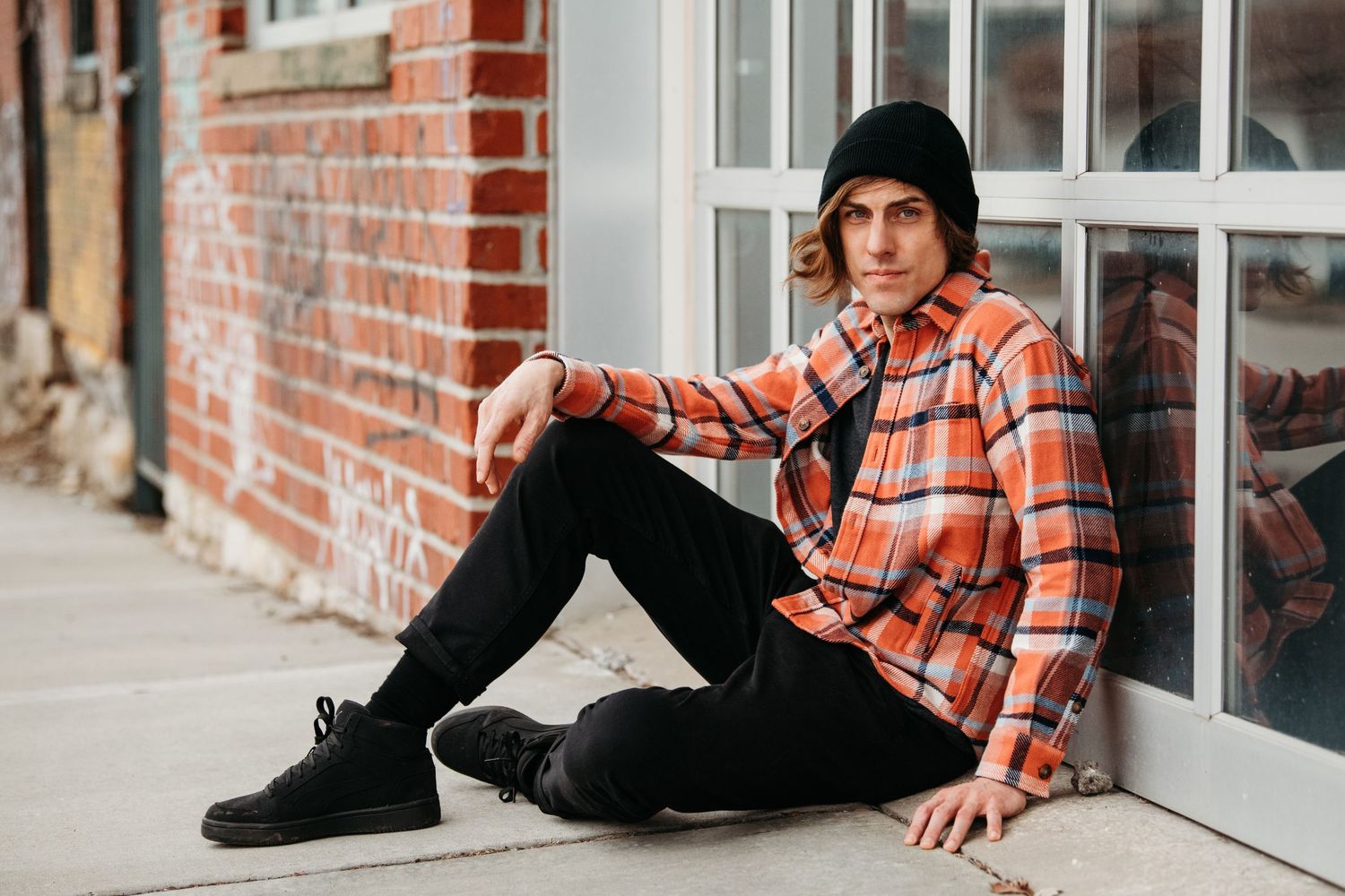 Urban portrait session with plaid shirt and beanie against brick building exterior.