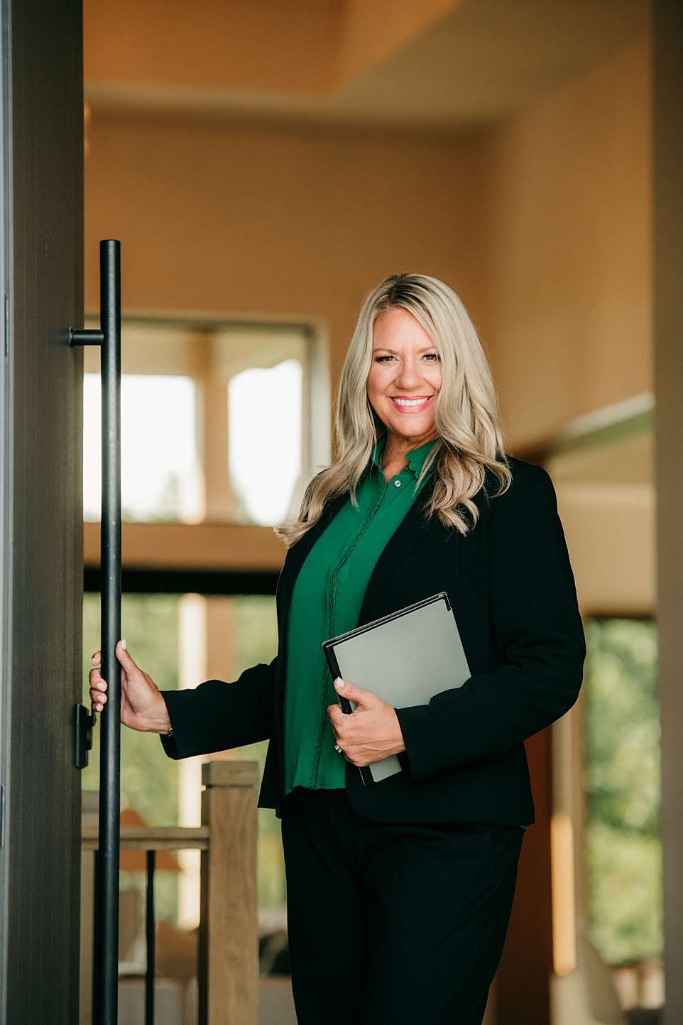 Professional wearing a black blazer and green scarf poses in four similar shots against an office interior background.