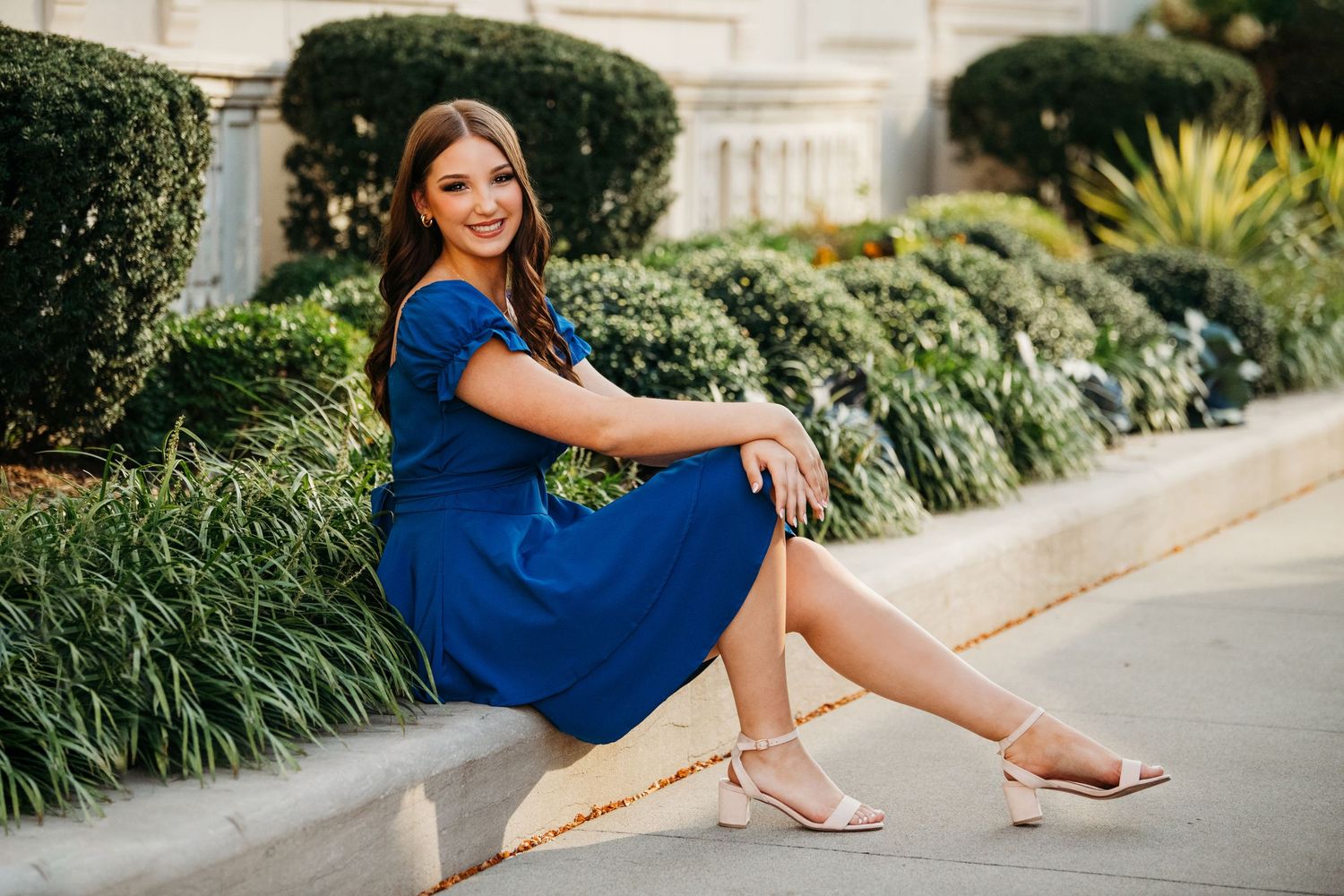 Fashion portraits in royal blue dress against landscaped garden setting.