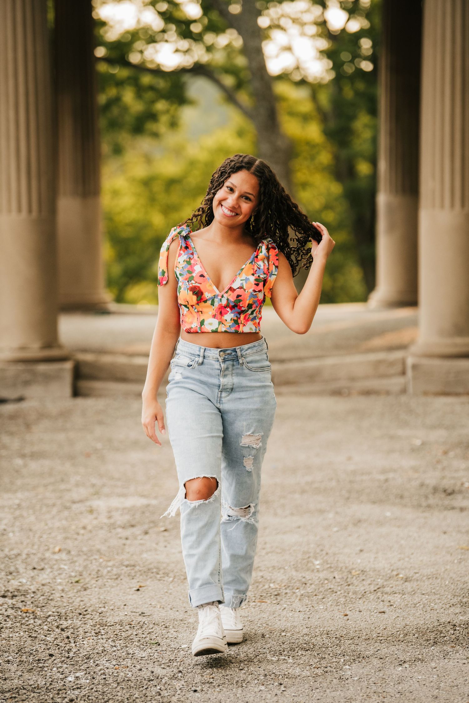 Casual portraits in floral top and distressed jeans near classical columns.