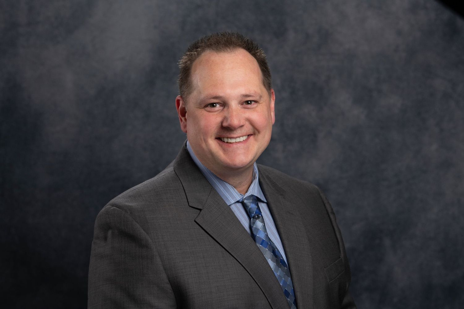 Professional corporate headshots of men in suits against dark backdrop.