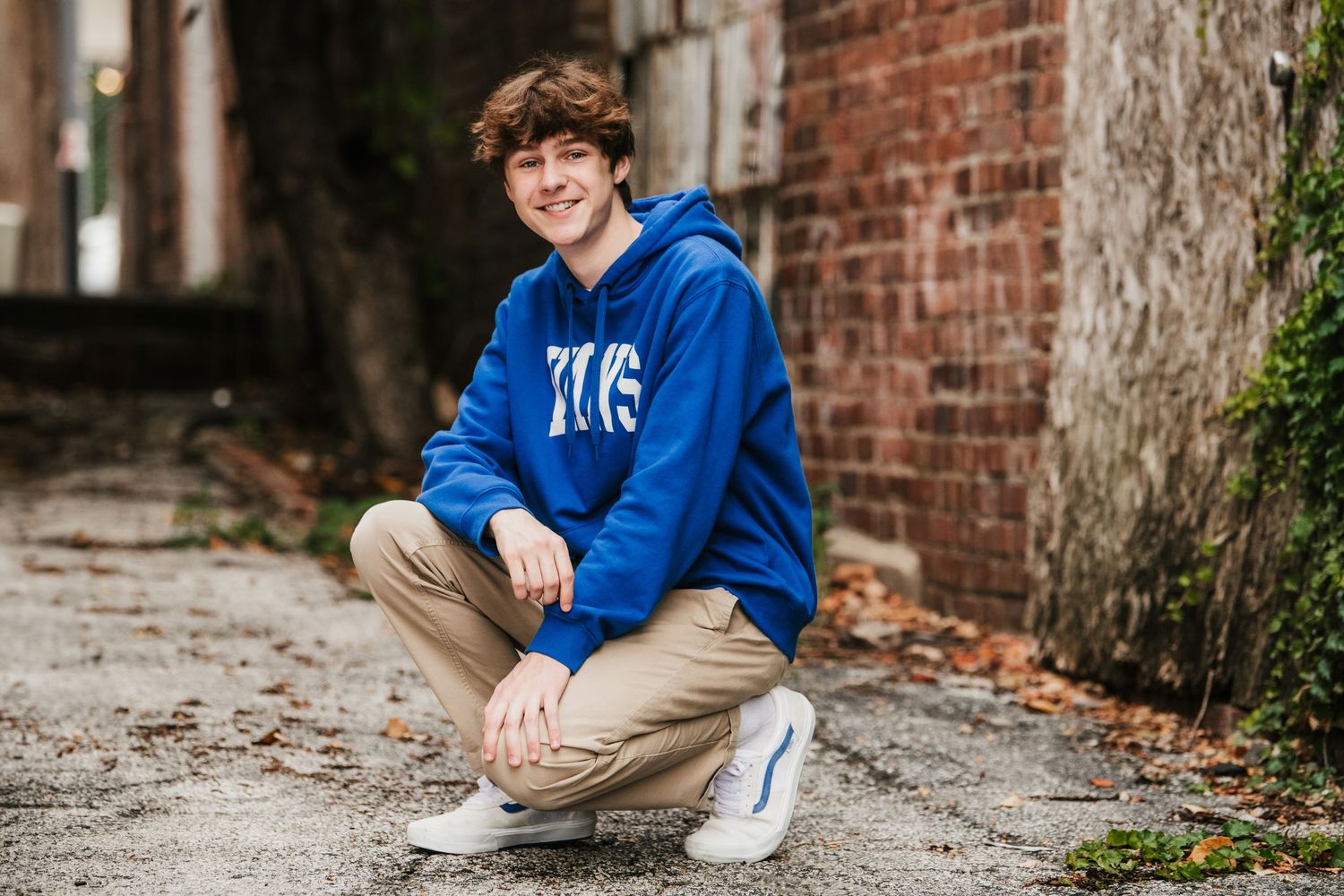 Casual portrait of someone in blue hoodie sitting against brick wall.