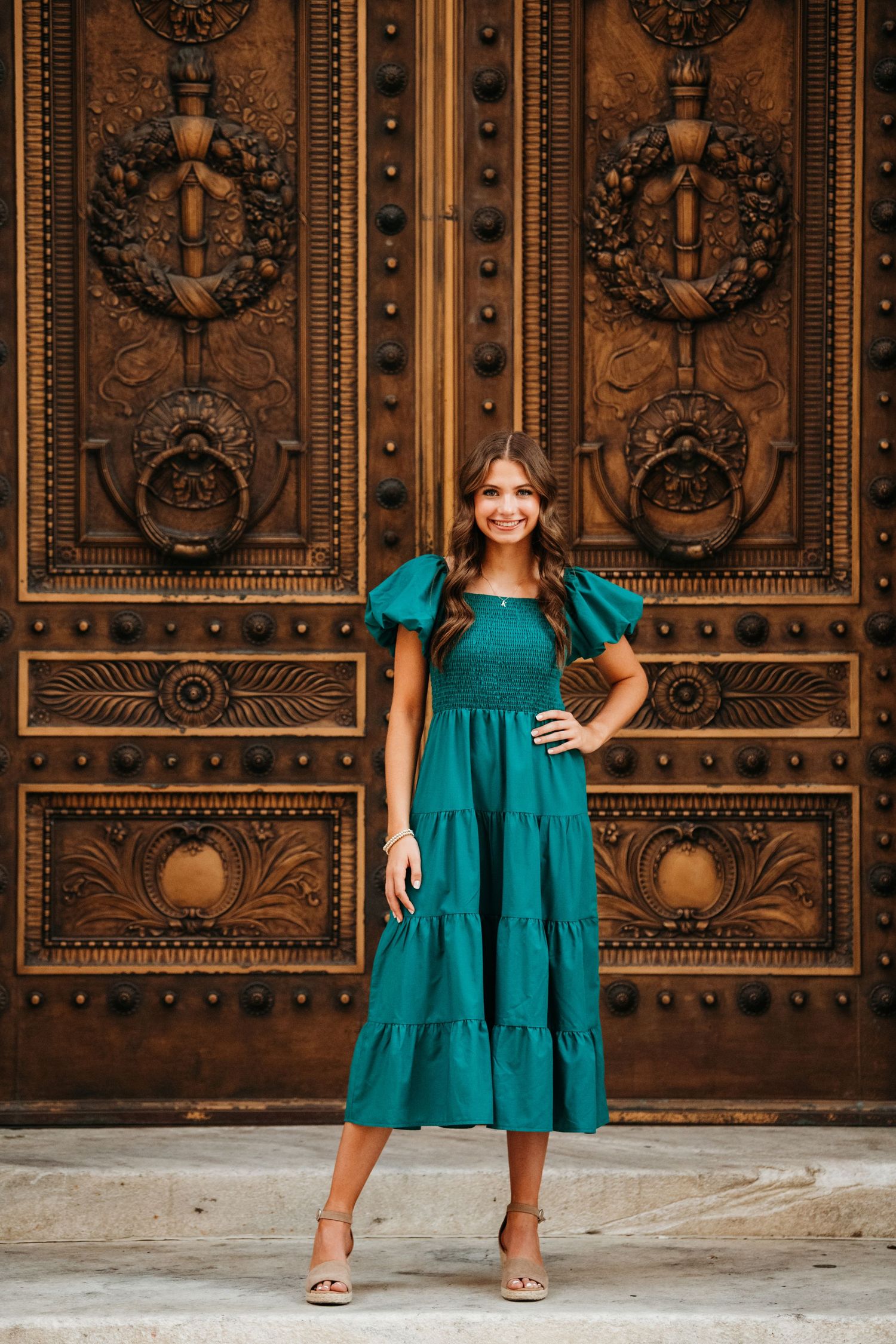 Portrait session in emerald green dress against ornate bronze doors with detailed metalwork patterns.