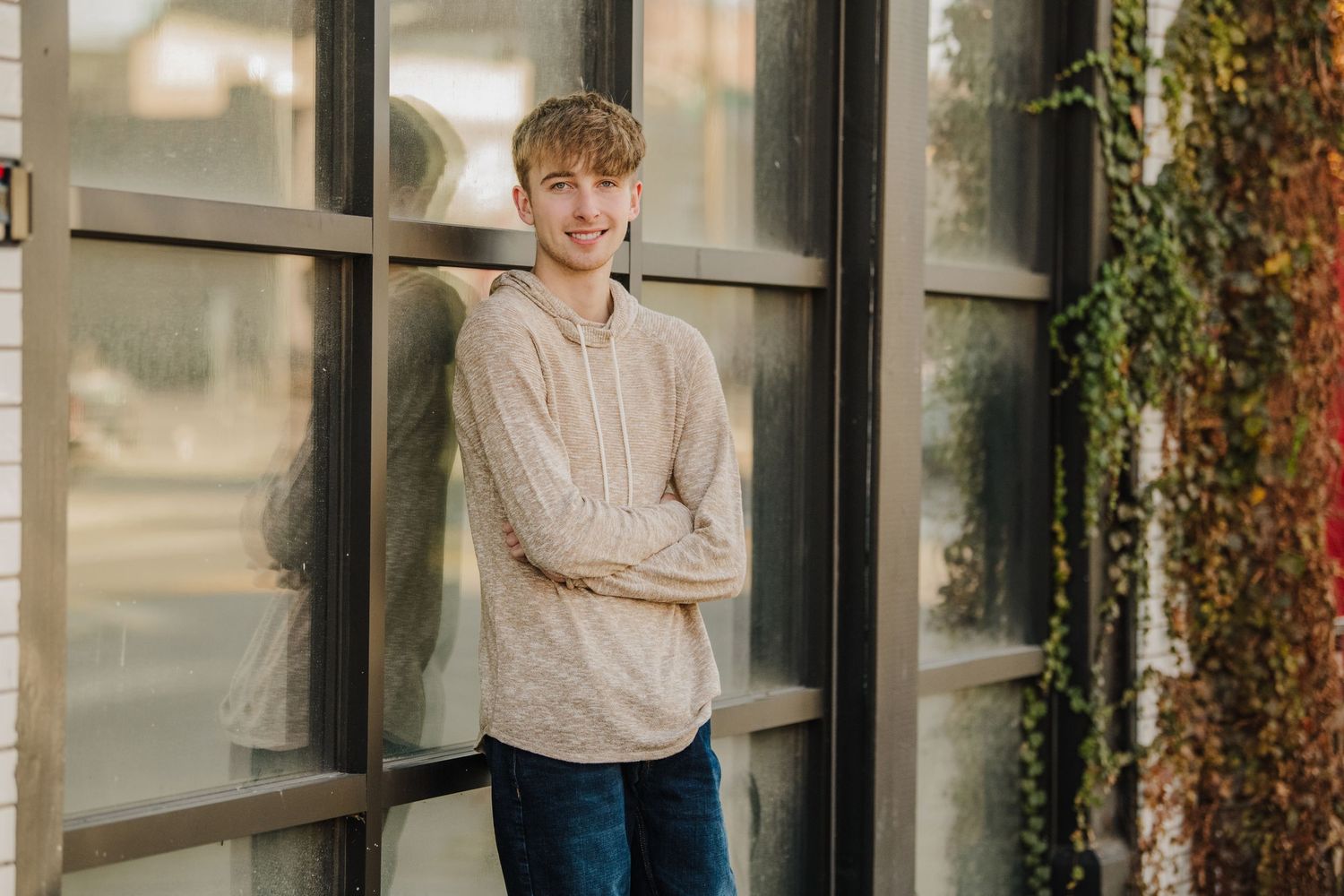 Person in casual attire poses against a brick wall with ivy in an outdoor portrait session.