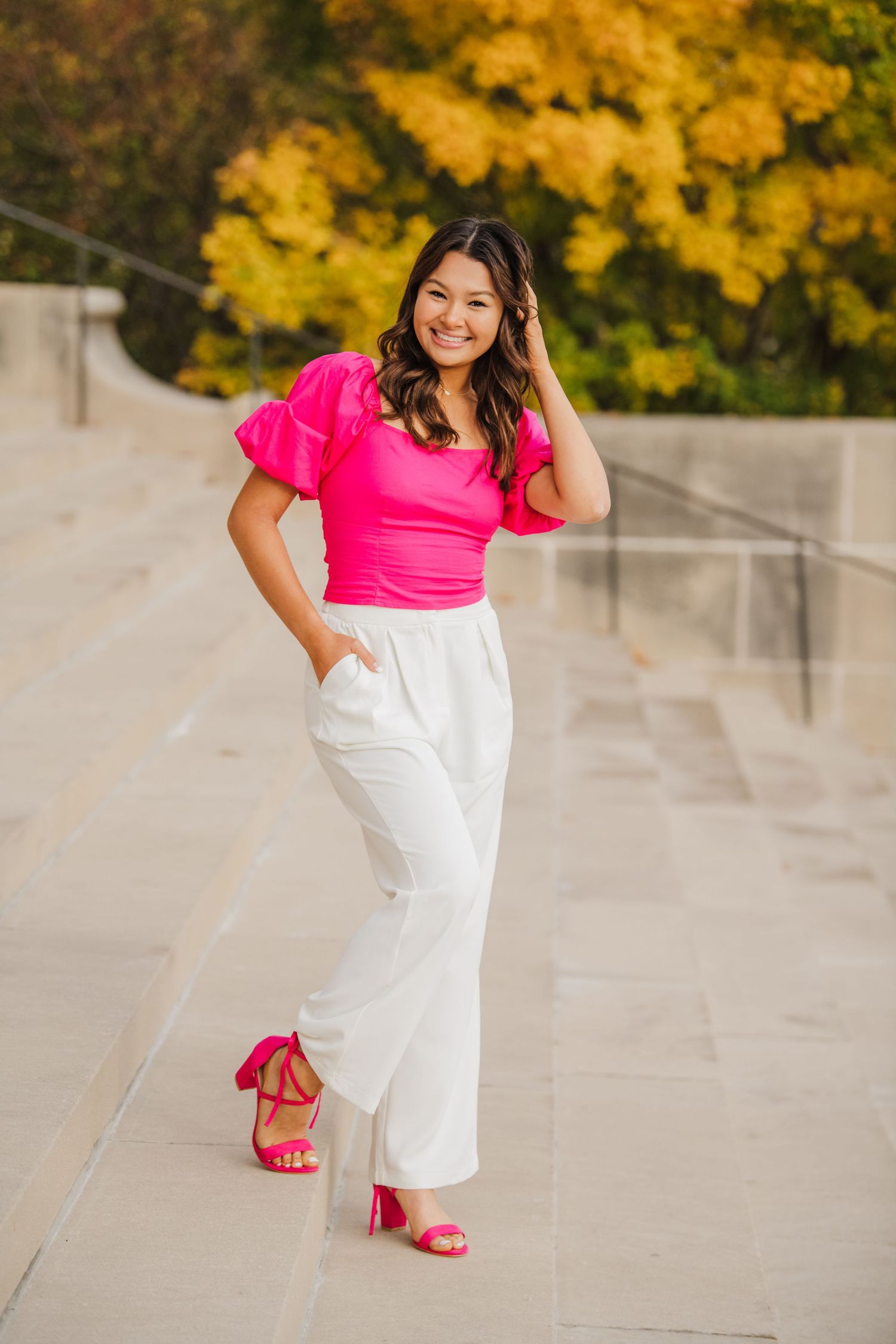 Fashion portraits in hot pink top and white pants with fall foliage backdrop.