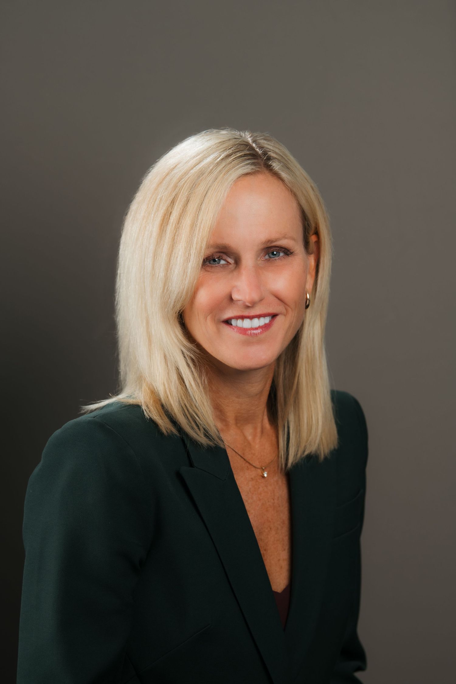 Professional headshot of woman in black blazer against neutral gray backdrop.