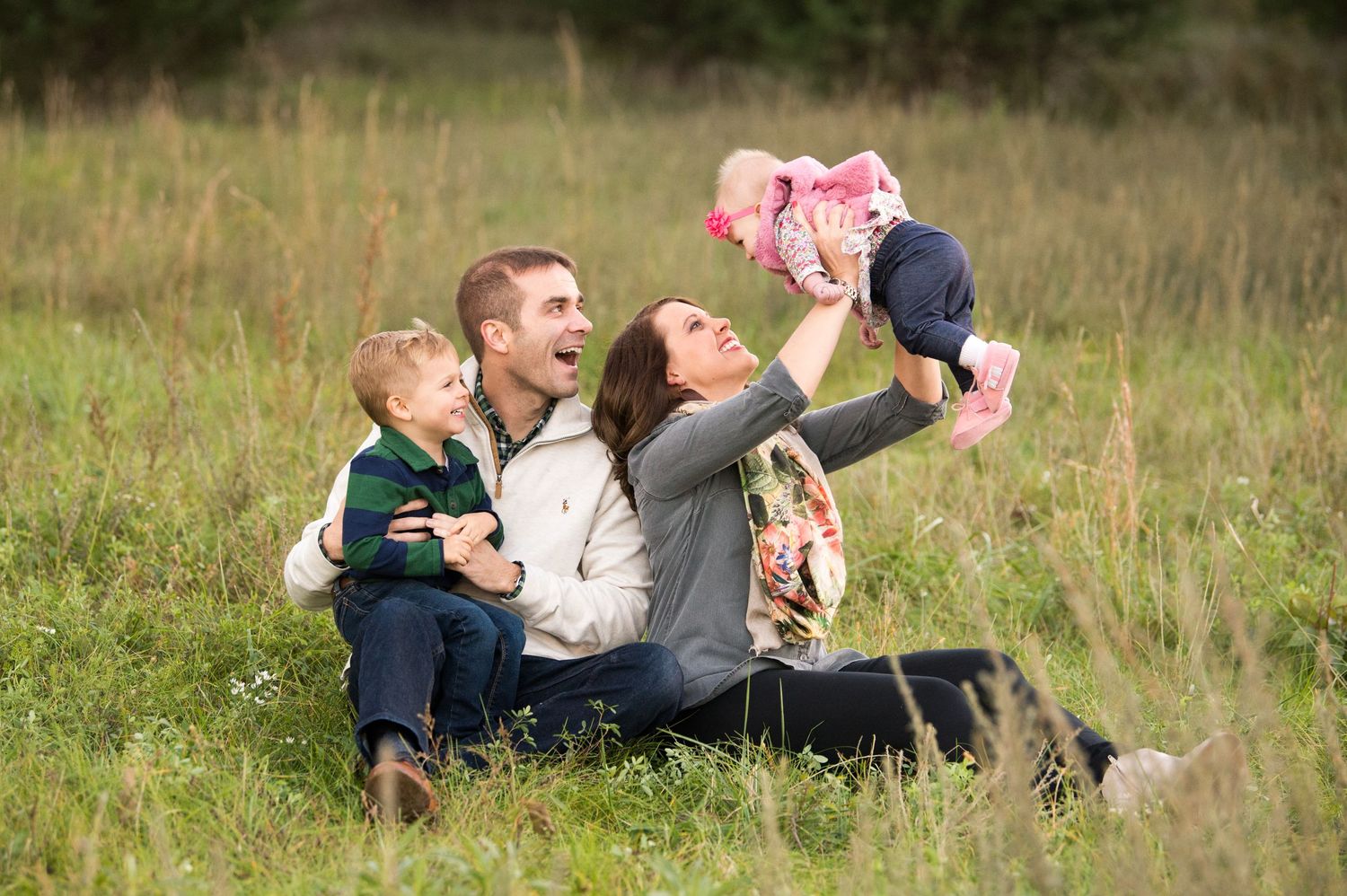 A family sits together in a grassy meadow playing and laughing while enjoying time outdoors.