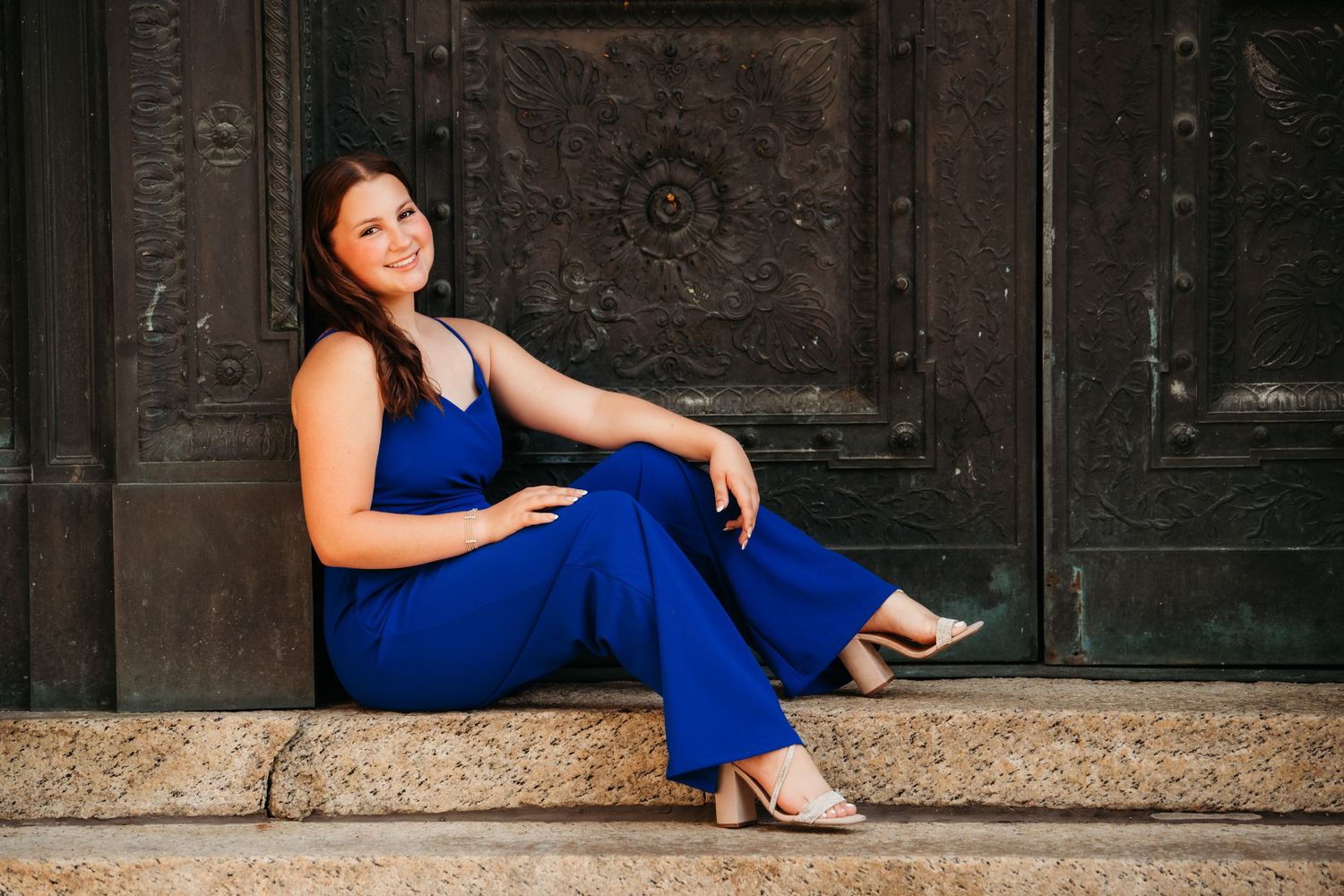 Person in royal blue outfit poses elegantly against dark vintage doors.