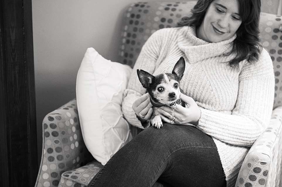 A person in a white sweater sits on a gray couch with a small dog.
