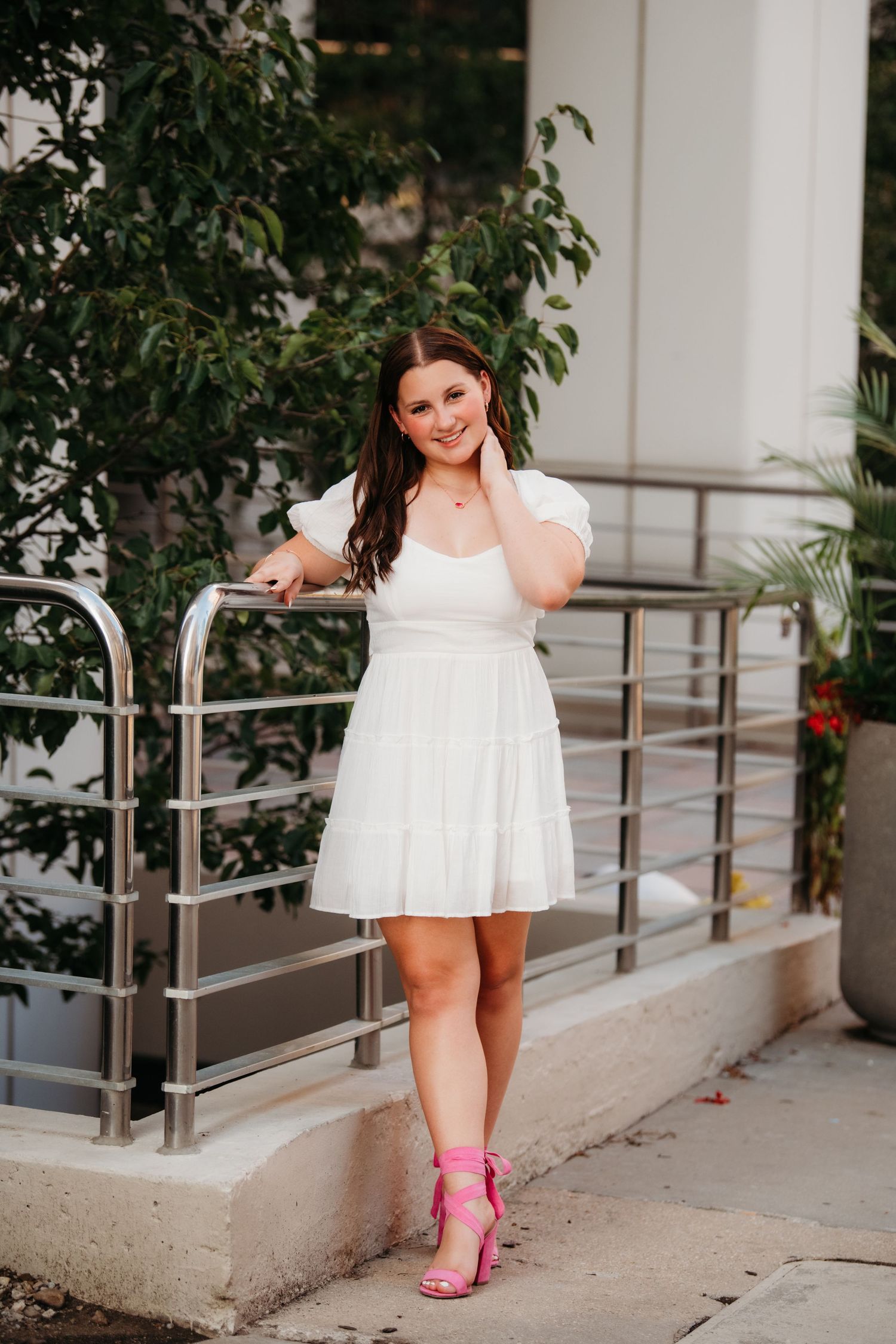 Fashion portraits in a white dress with pink boots against modern architecture with glass and railings.