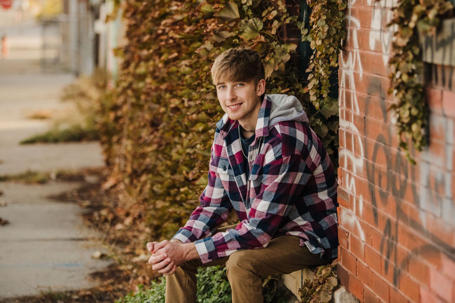 Casual autumn portraits in plaid shirt against brick wall with ivy.