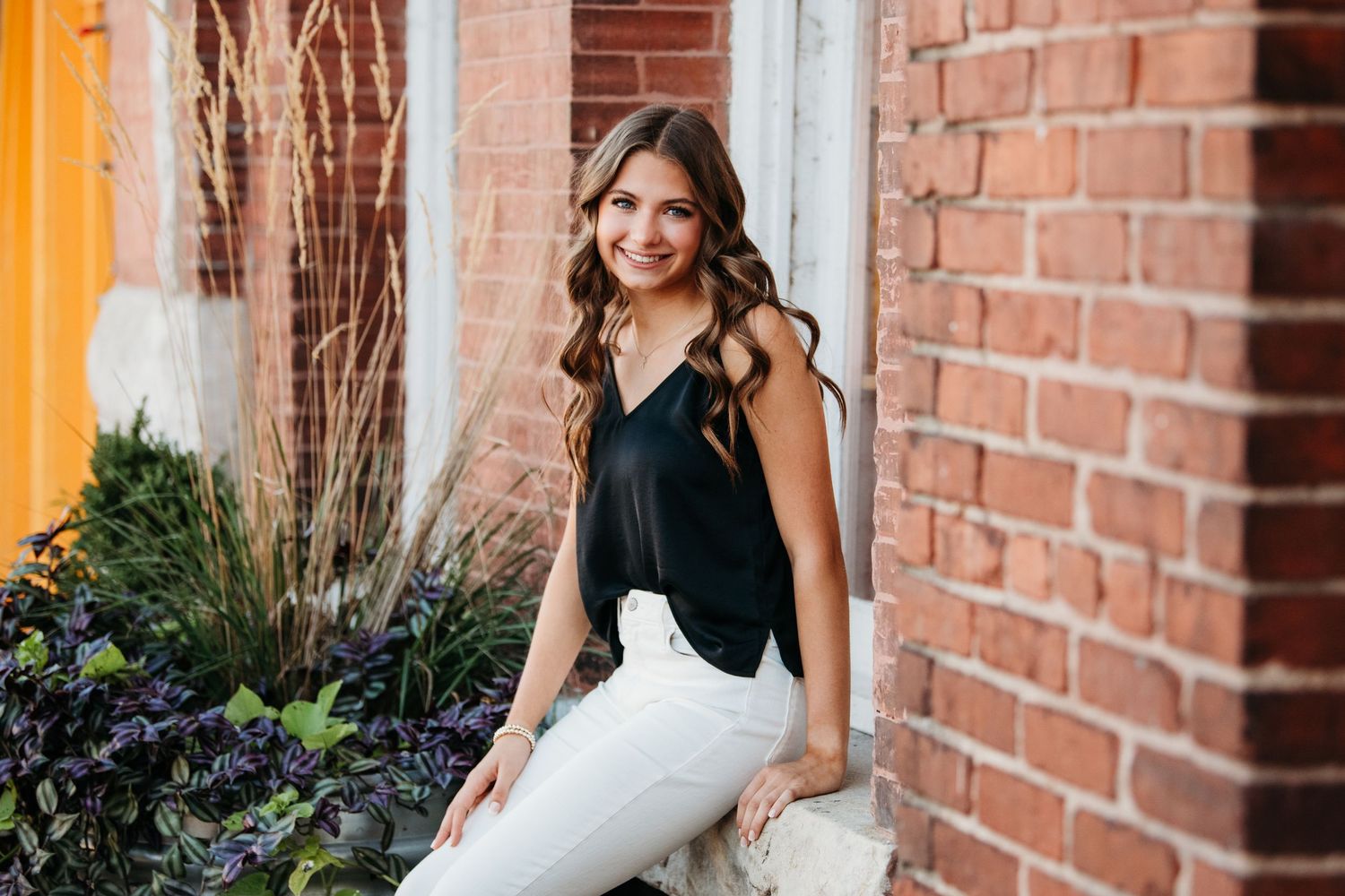 Elegant portrait session against brick wall with floral arrangements and natural lighting.