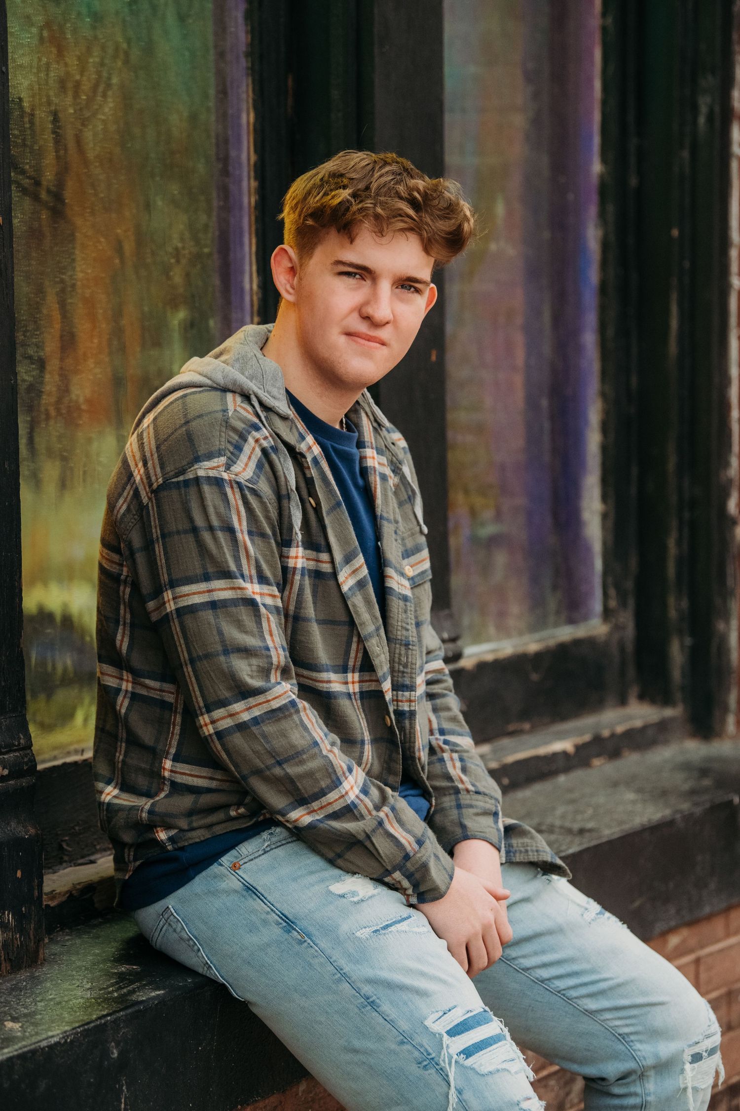 Person in plaid shirt and jeans sitting casually on outdoor steps.
