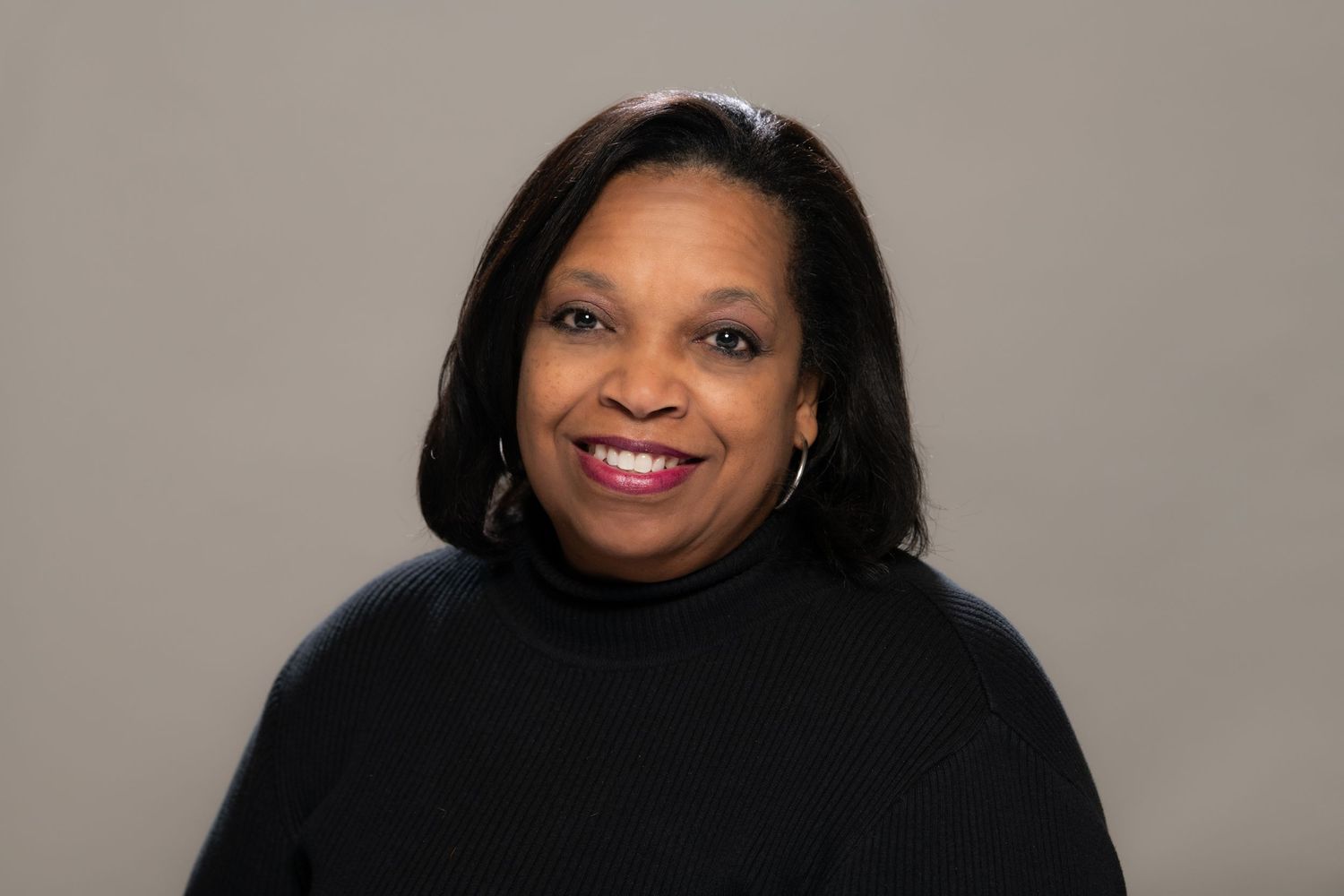 Professional headshot of woman in black outfit against neutral gray background.
