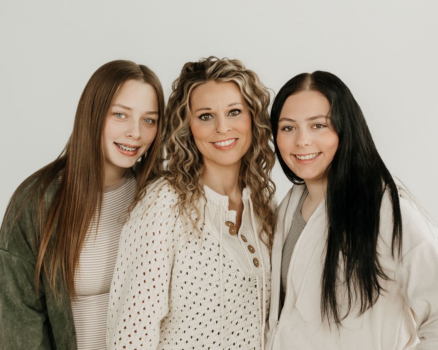 family photo with two older girls and mom on a white backdrop