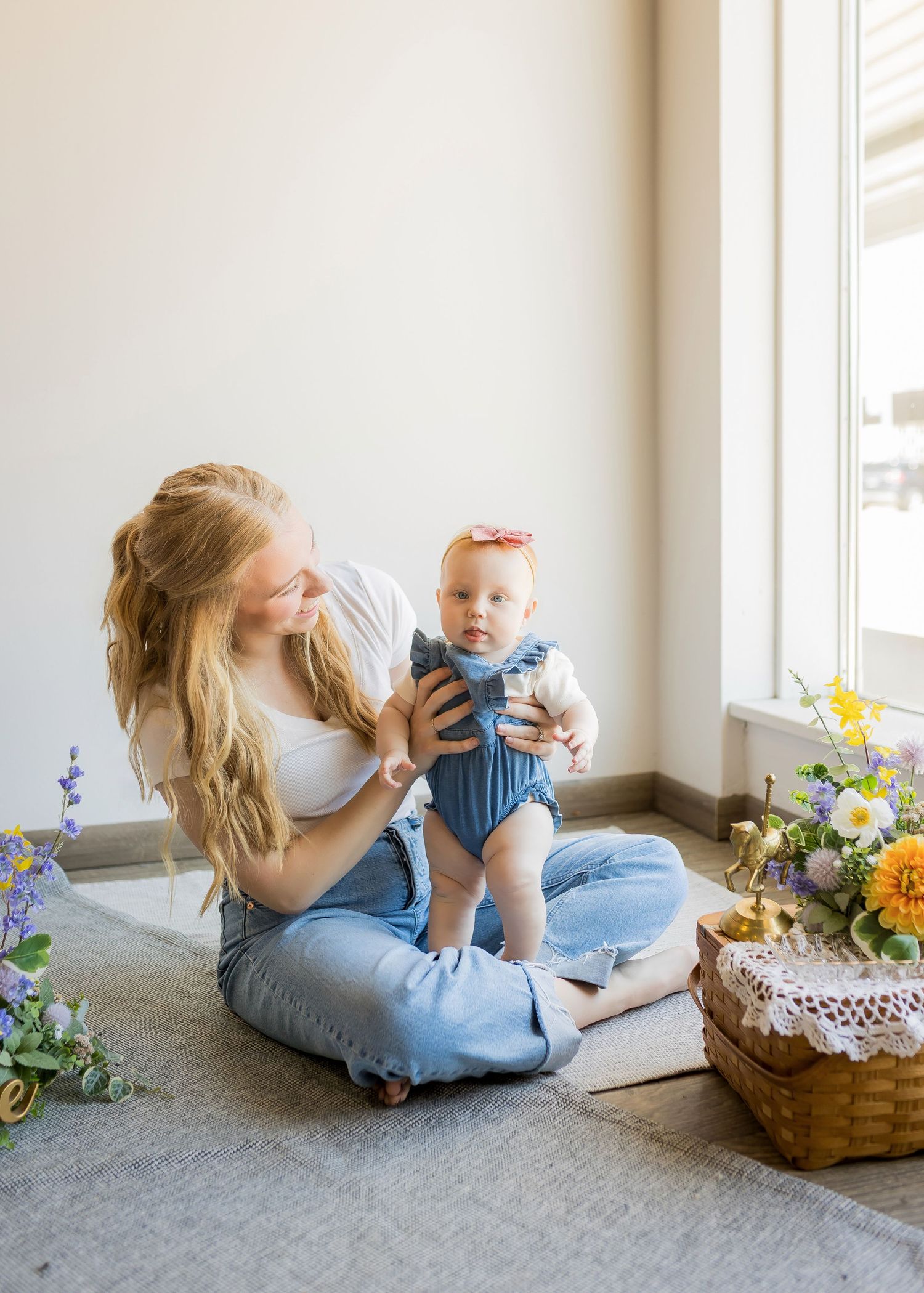 Parent and baby sharing tender moments by a window with flowers in a basket.