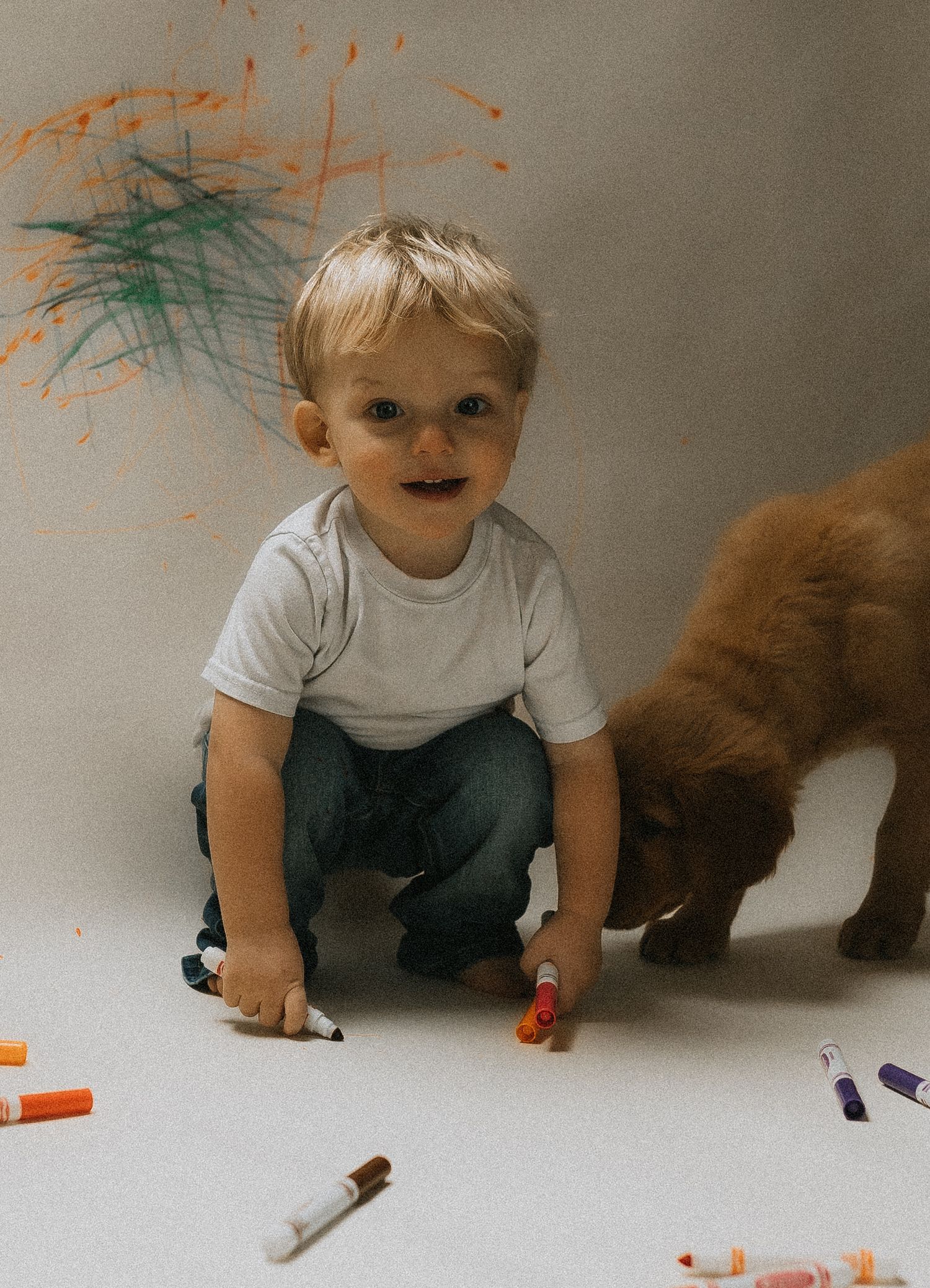 Young child drawing with colorful markers on paper while sitting on the floor with his puppy