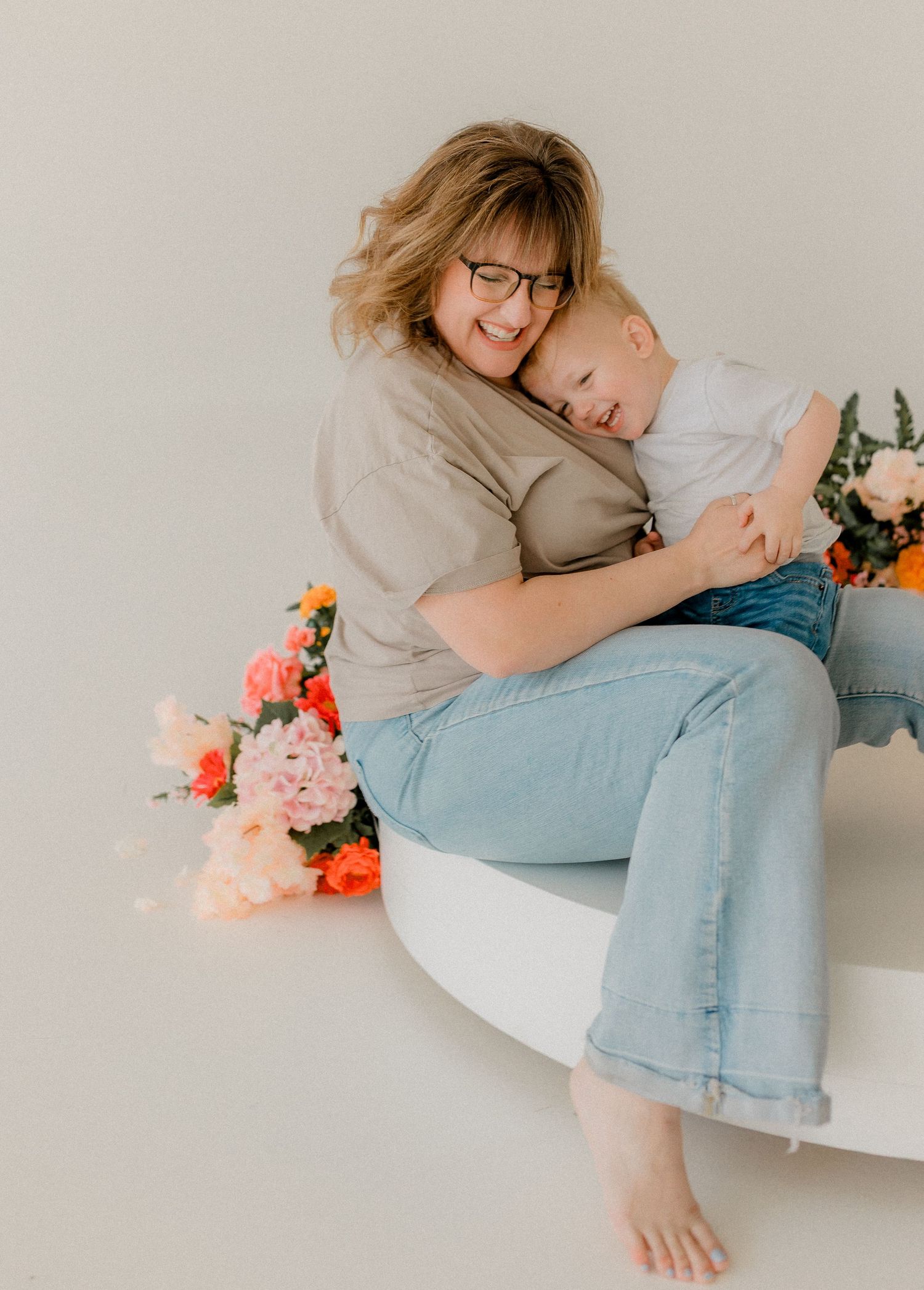 Person in casual attire lounging on white furniture with colorful flowers nearby.