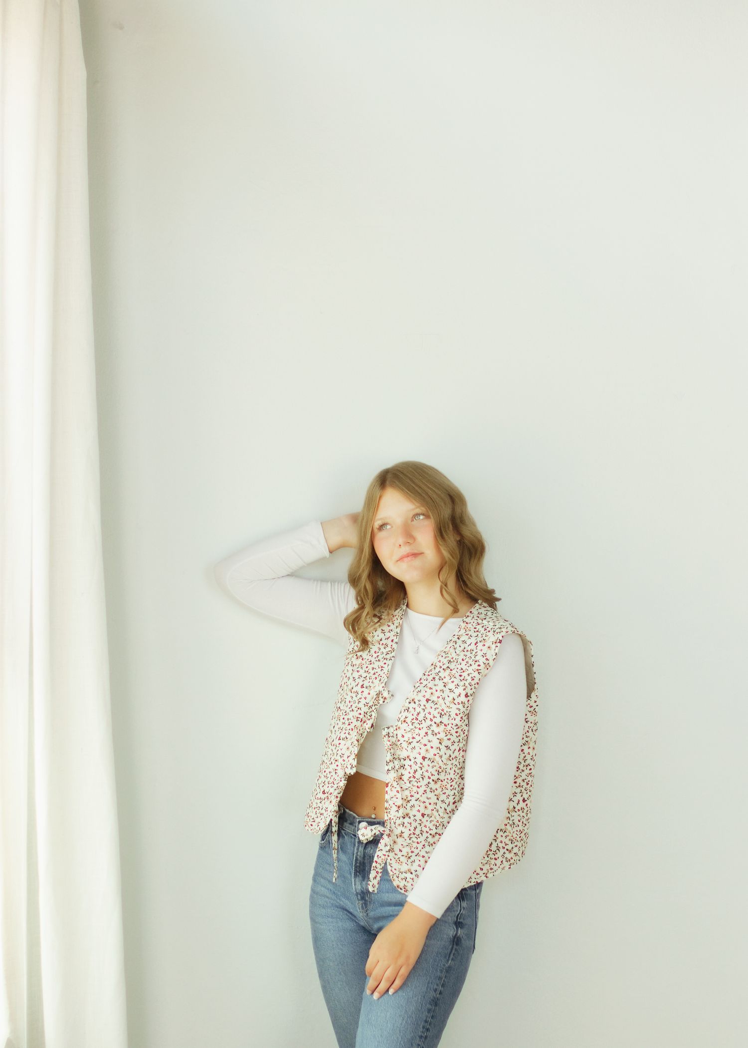 Woman in leopard print vest, white top, and jeans posing against a light gray wall.