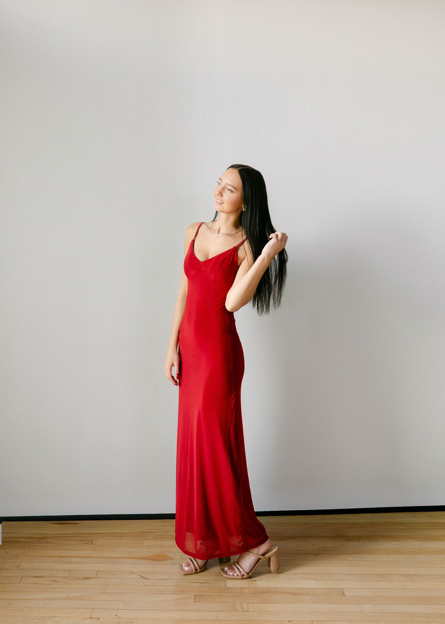 Woman in elegant red satin maxi slip dress with spaghetti straps, paired with nude heeled sandals.