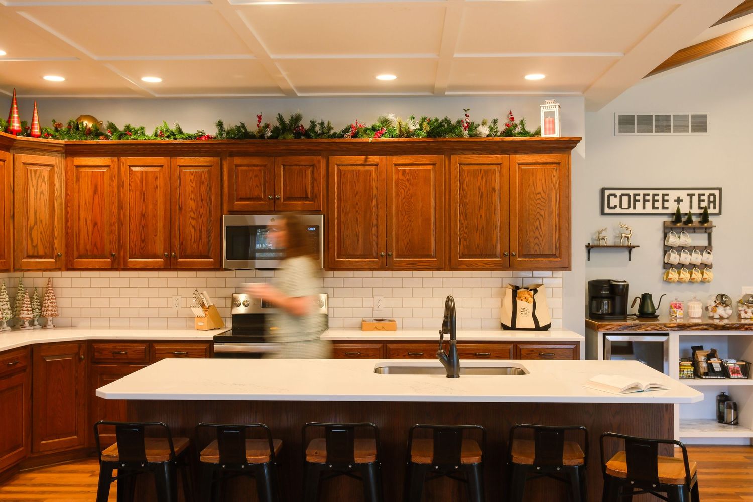 Modern kitchen with wood cabinets, white island, bar stools, subway tile backsplash, and a coffee and tea station.