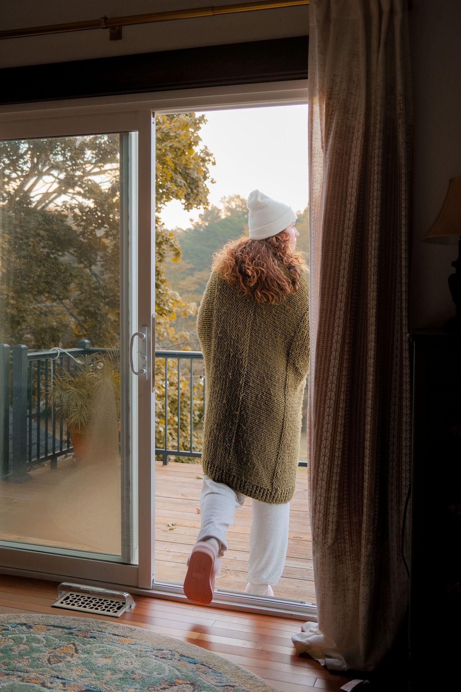 Person in knit sweater standing on balcony looking at autumn scenery.