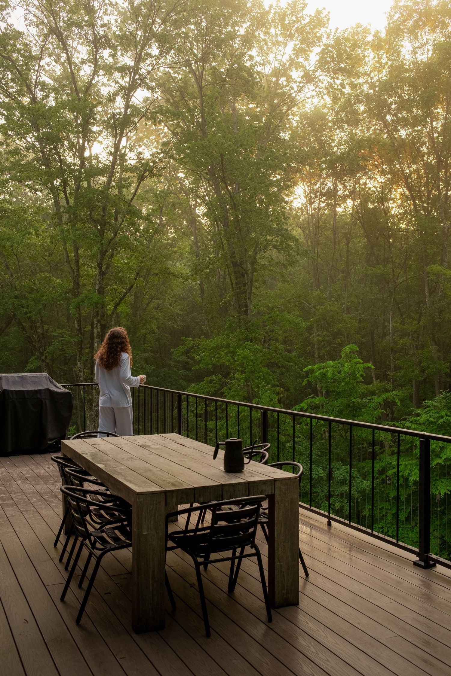 Wooden deck furniture set against backdrop of green forest canopy during golden hour.