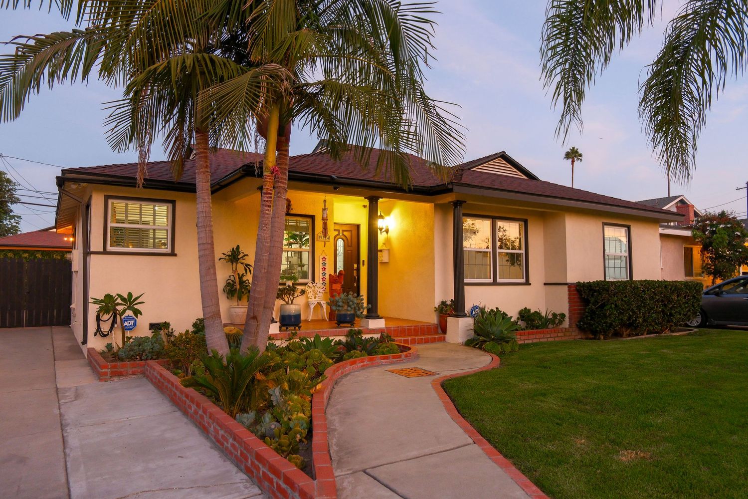 Charming ranch-style home with palm trees, warm porch lighting, and lush landscaping at dusk in a California neighborhood.
