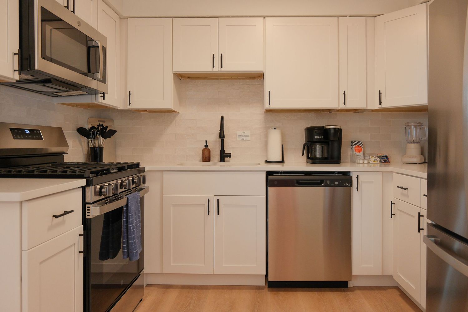 Modern white kitchen with stainless steel appliances, shaker cabinets, subway tile backsplash, and hardwood floors.