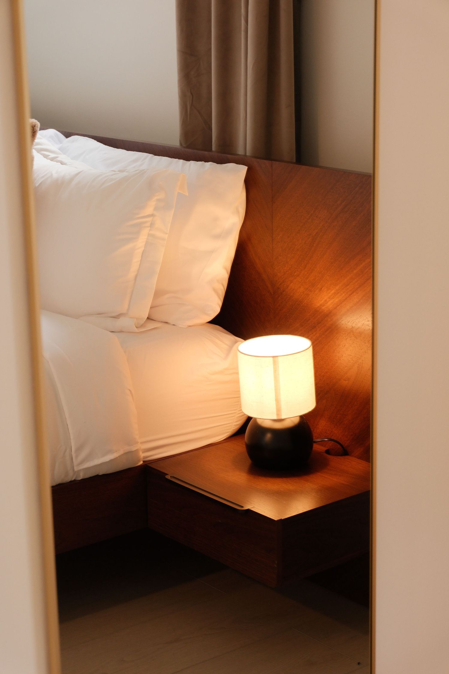 A cozy bedroom with white pillows on a wooden bed and a glowing bedside lamp on a nightstand.
