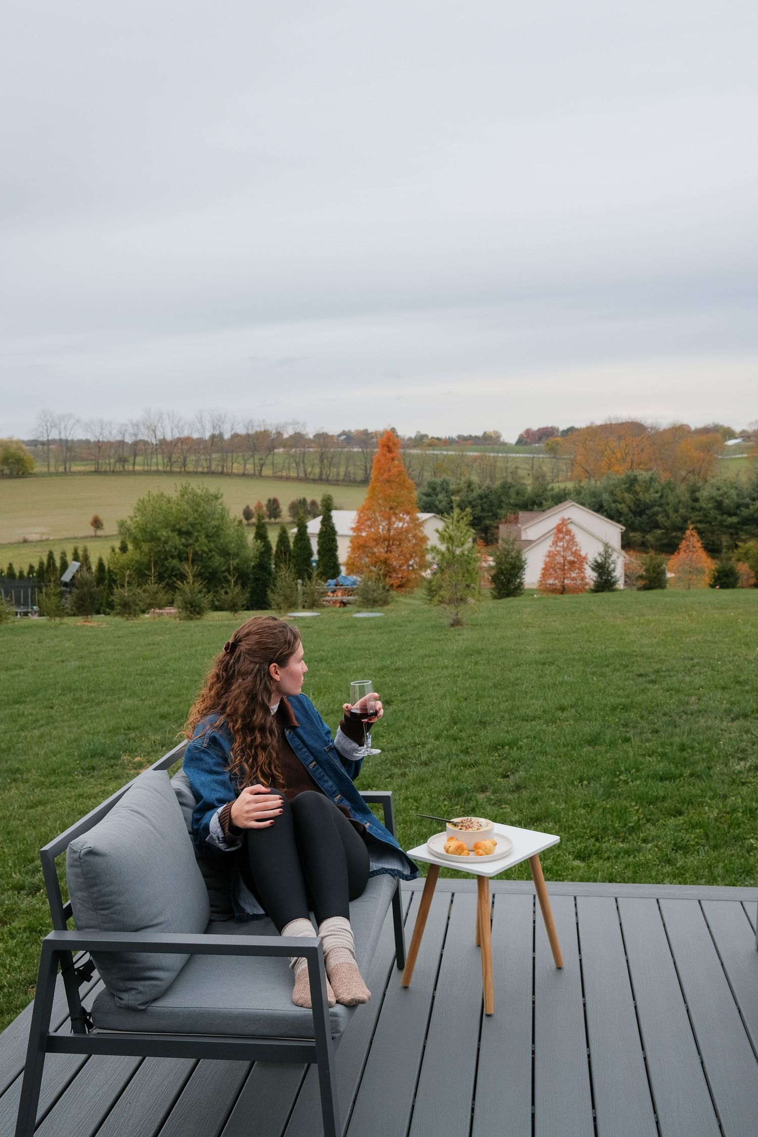 People relaxing on outdoor deck furniture overlooking rural farmland and autumn trees.
