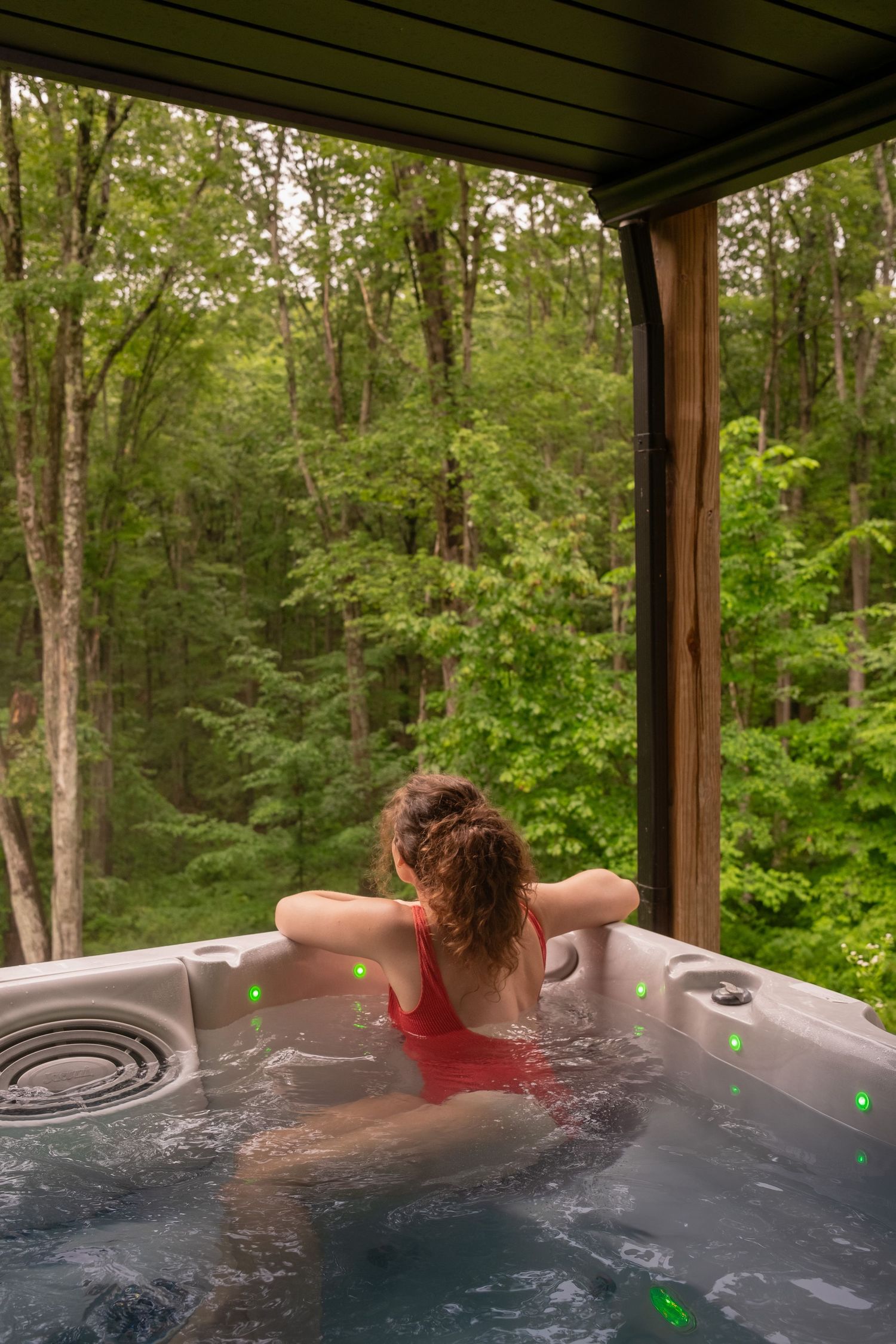 Outdoor hot tub overlooking a lush green forest with steam rising from the water.