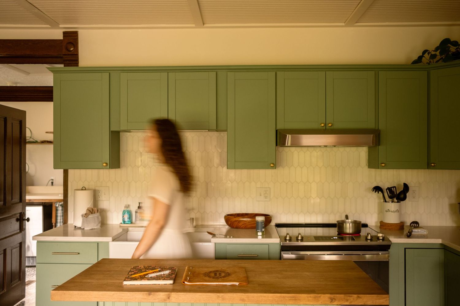 Modern kitchen interior with sage green cabinets and wooden accents in natural lighting.