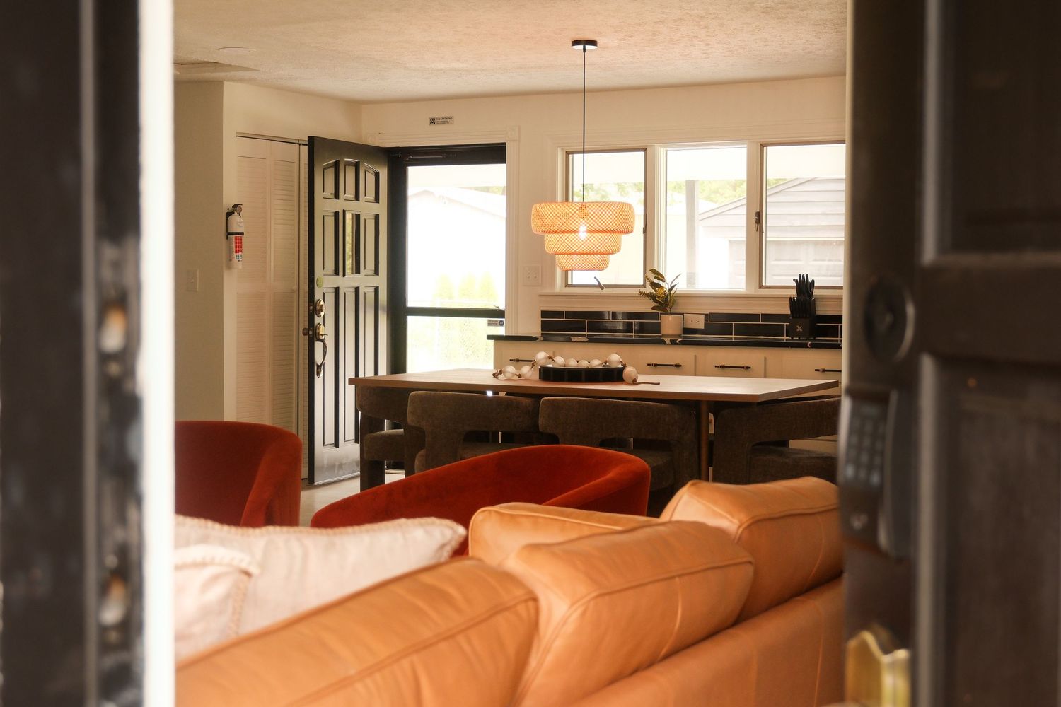 Warm living room with orange leather sofa opening to dining area with pendant light and modern kitchen beyond.
