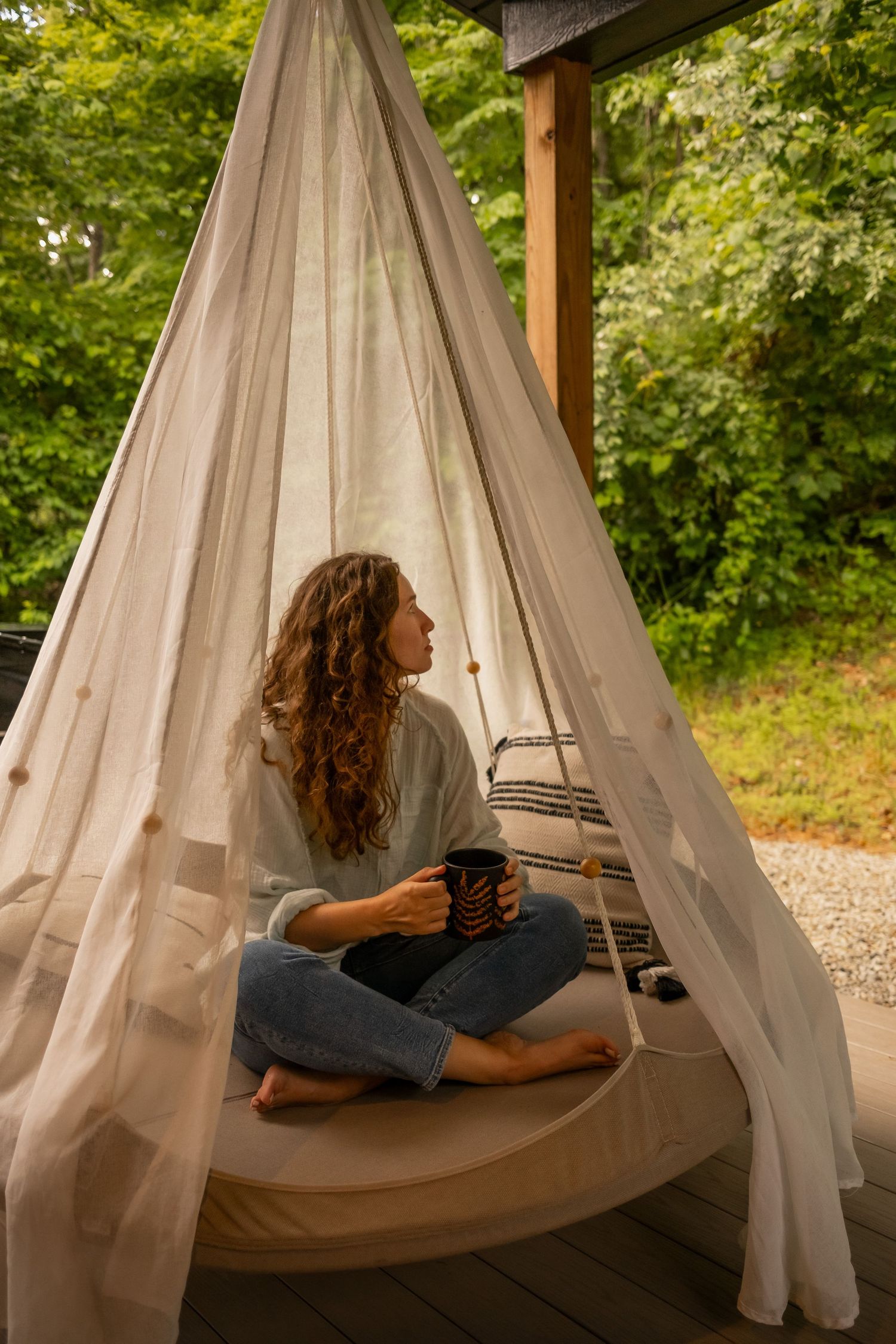Hanging outdoor daybed with white curtains surrounded by green foliage.