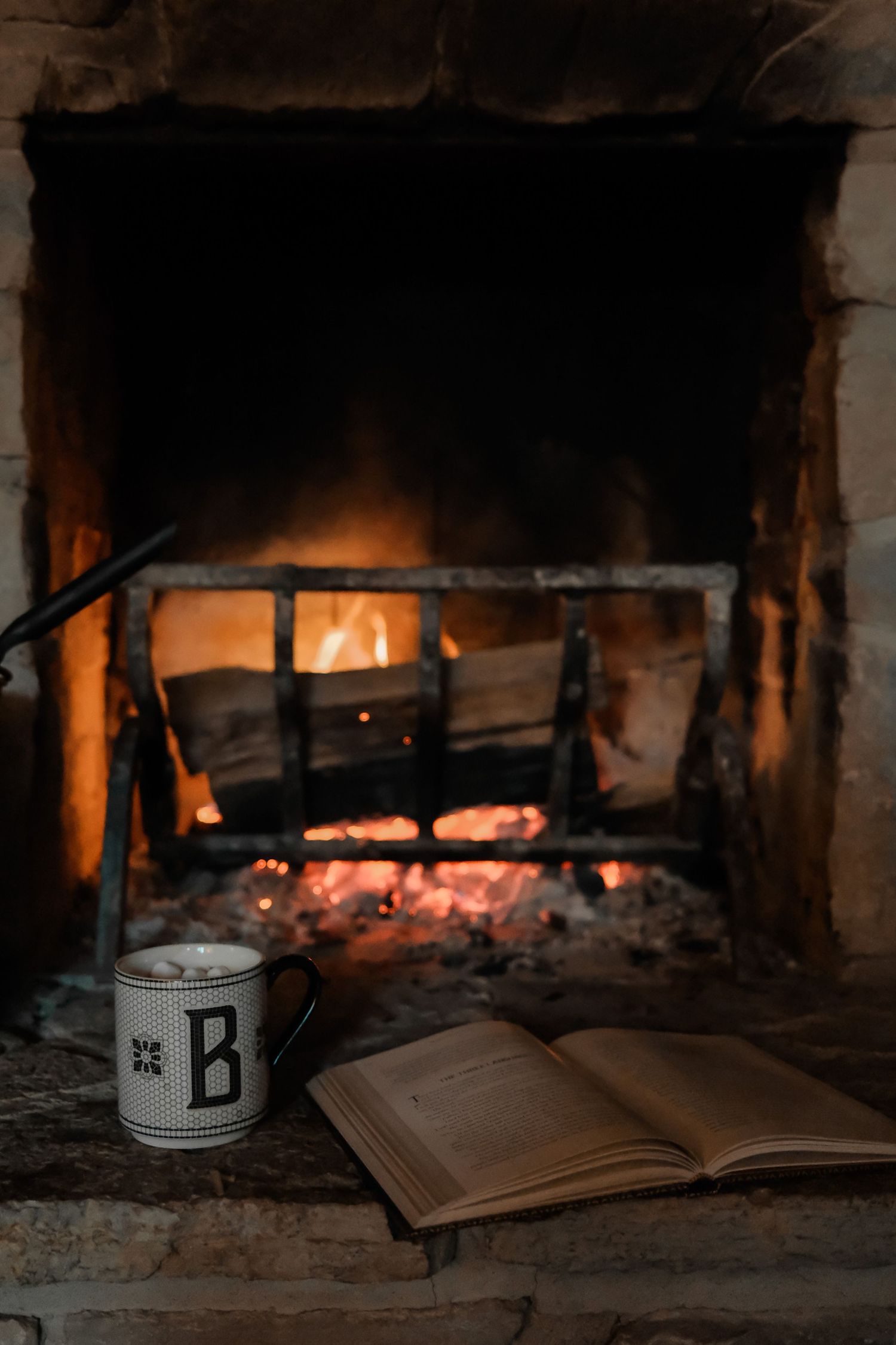 Open book and mug beside a crackling fireplace creating a cozy reading atmosphere.