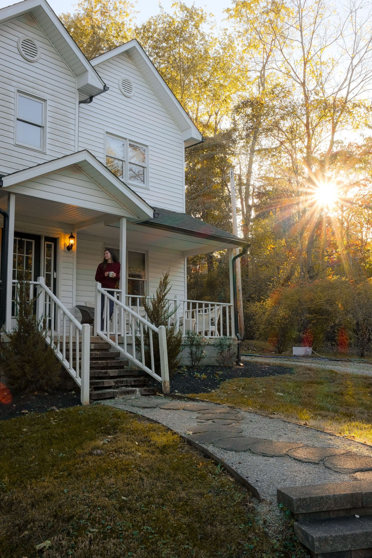 White farmhouse with wraparound porch captured during golden hour with fall foliage.