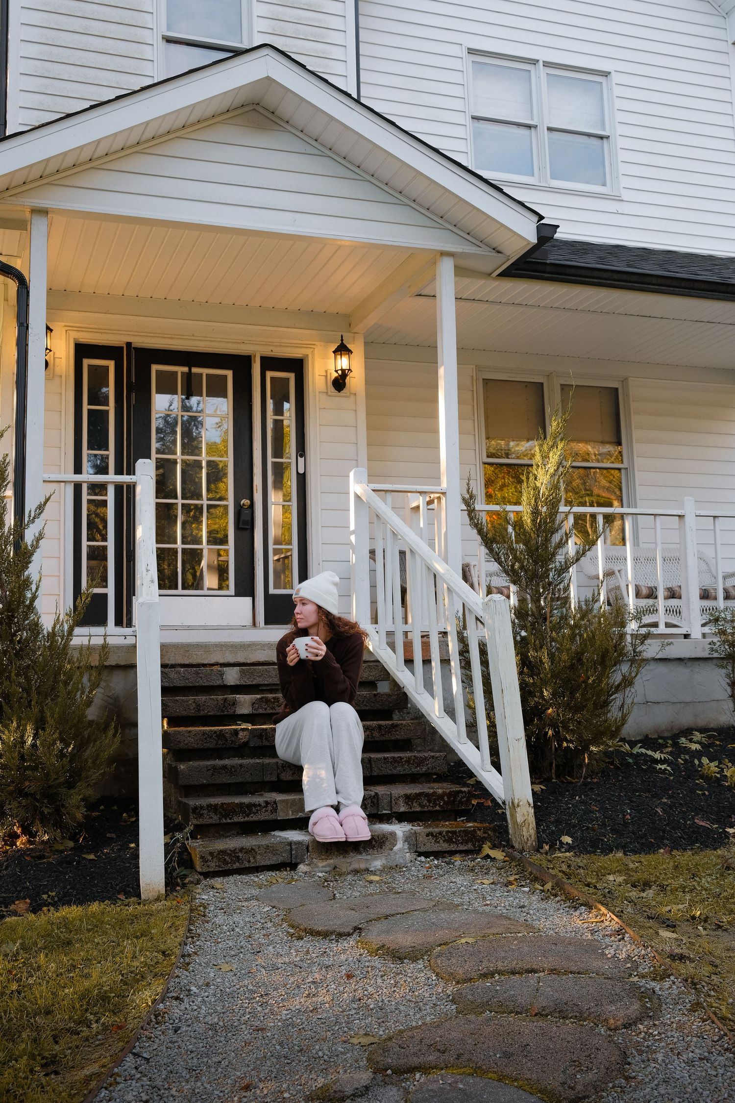 White farmhouse porch with wooden steps and railings surrounded by autumn landscaping.