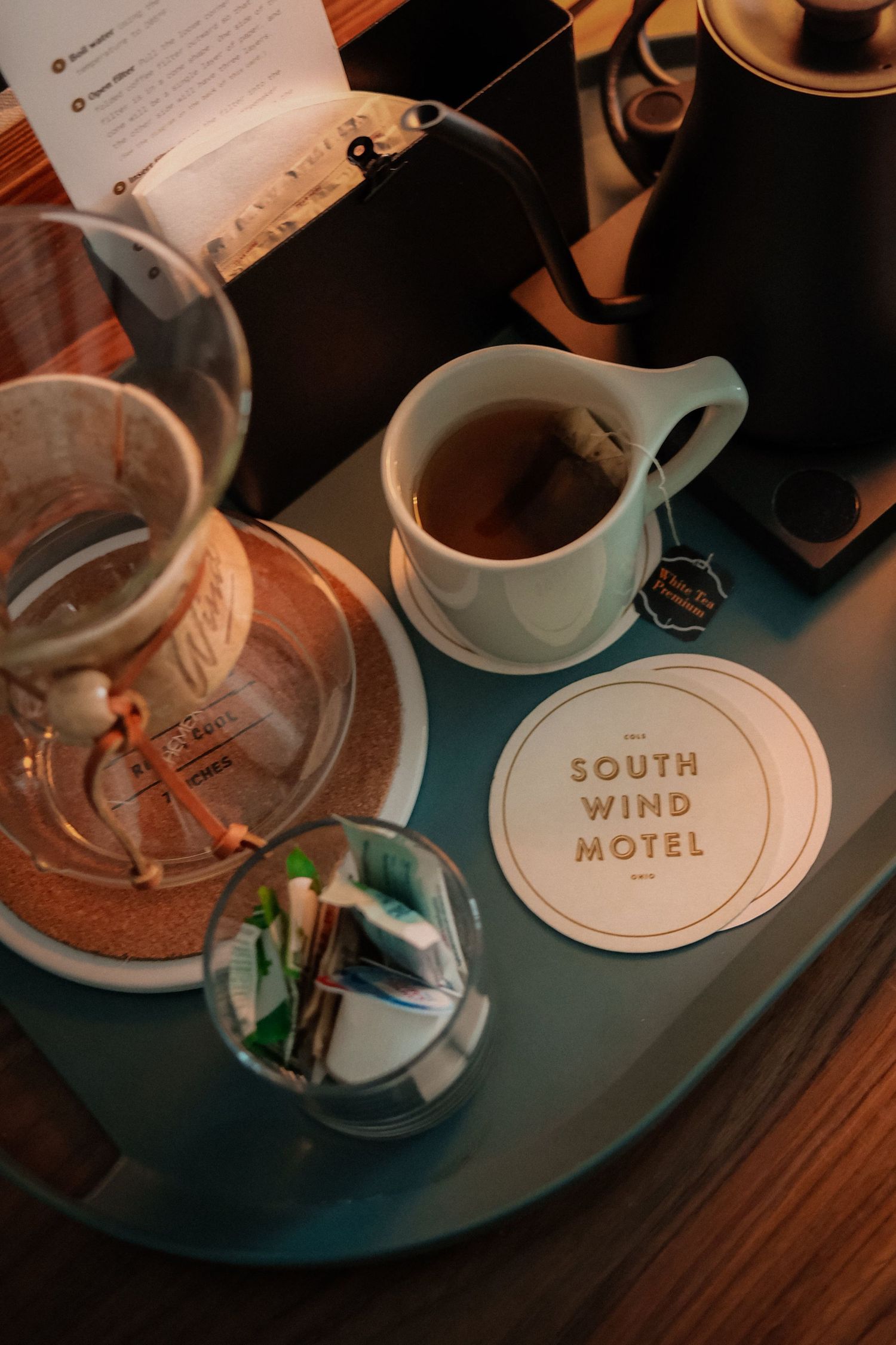 Coffee cups and branded coasters from South Wind Motel arranged on dark wooden surface.