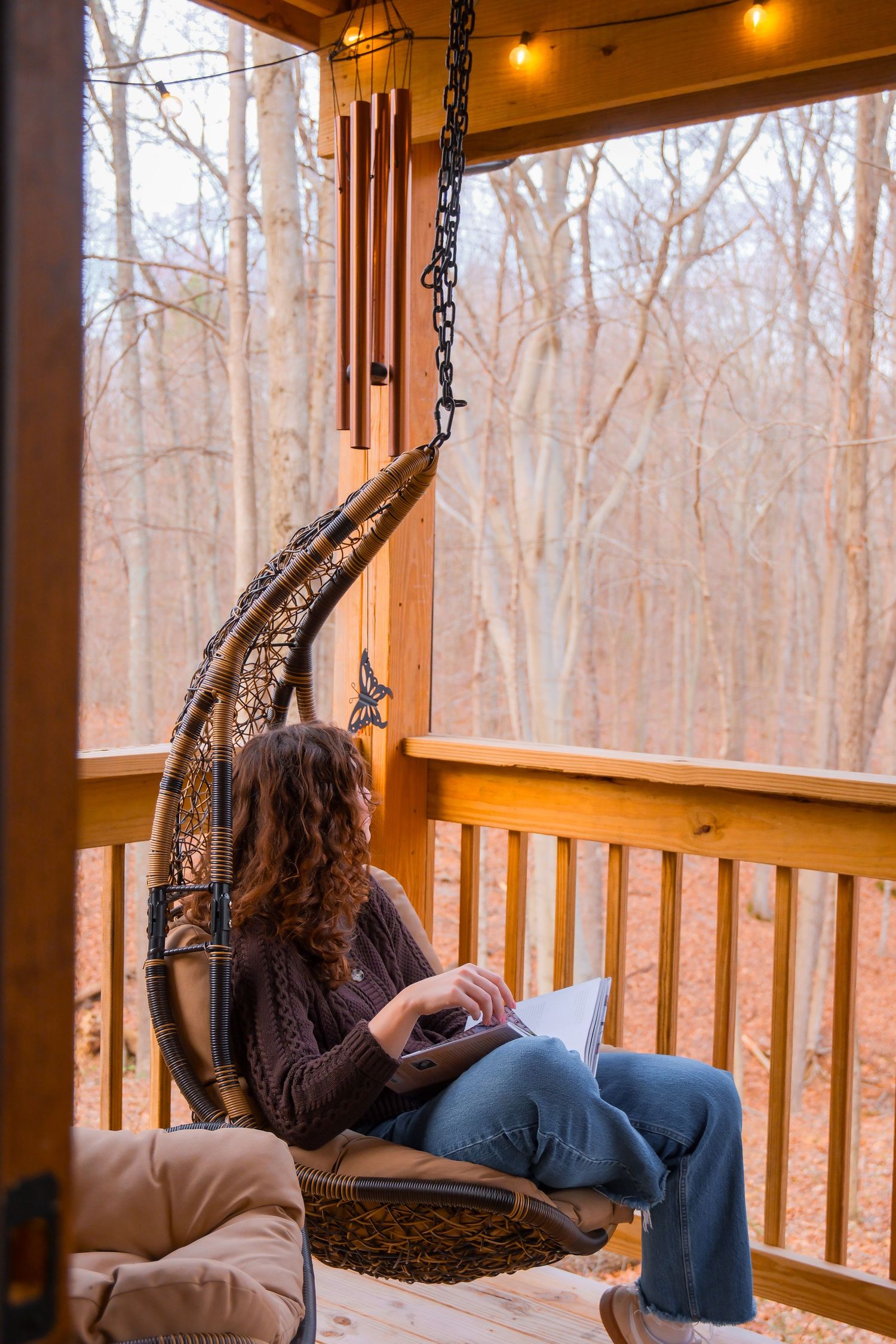 Woman relaxing in crescent moon hanging chair on wooden porch surrounded by autumn forest trees.